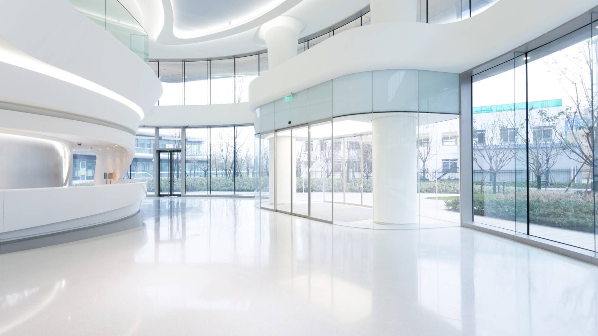 Bright, modern white lobby with curved structures, large windows, and glossy floors.