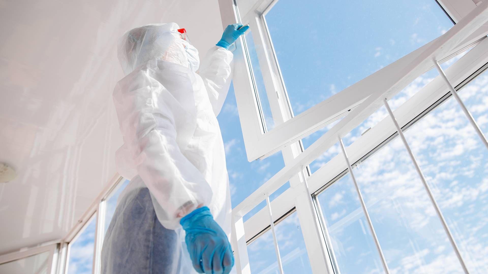 Person in protective suit inspecting window. Blue sky visible.