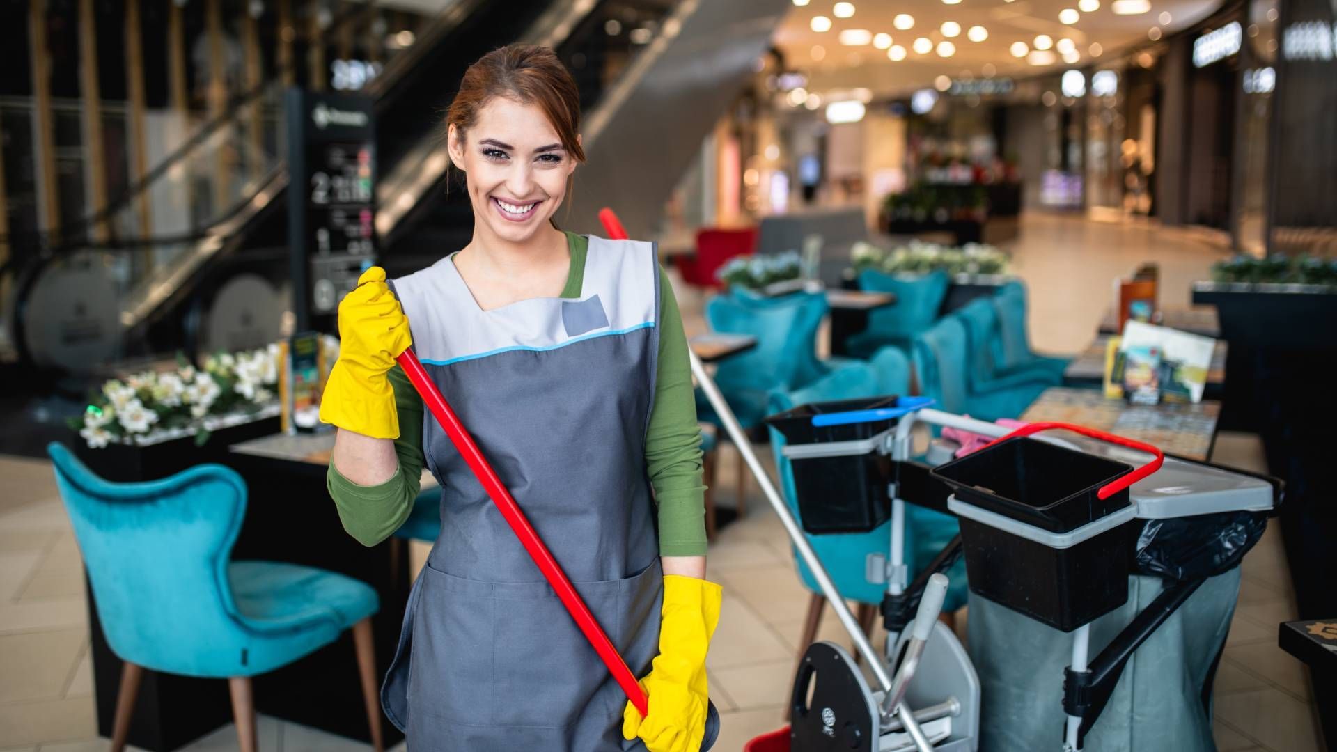 Smiling cleaning worker in yellow gloves, with a mop, in a shopping mall.
