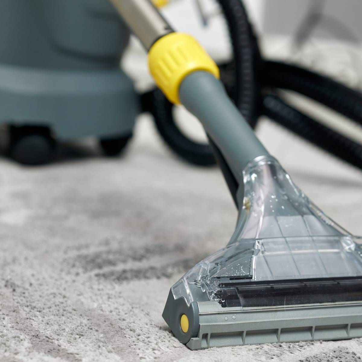 Carpet cleaner nozzle over a light gray carpet, with yellow and gray accents.