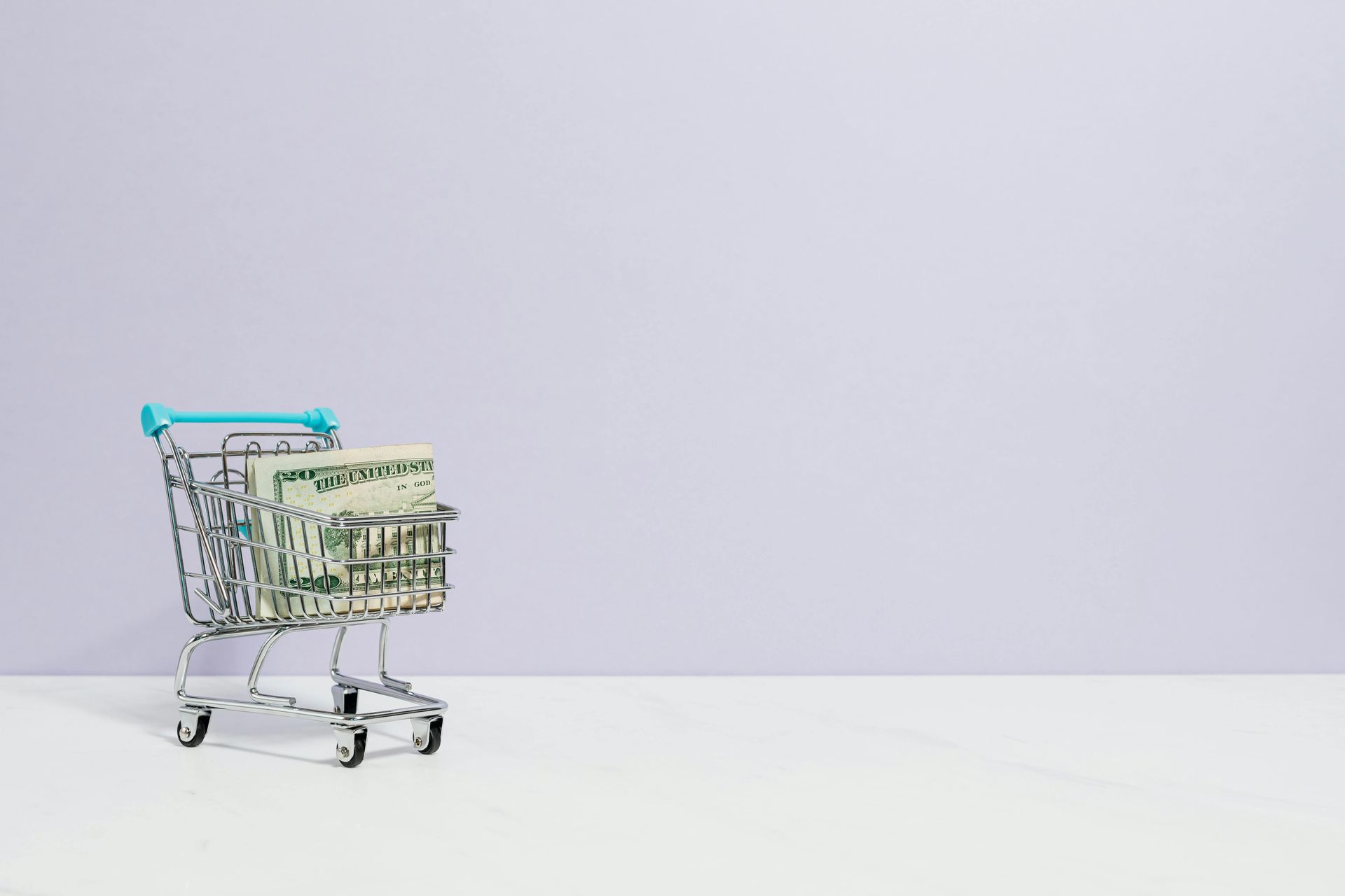 Shopping cart filled with money on a white surface against a purple background.