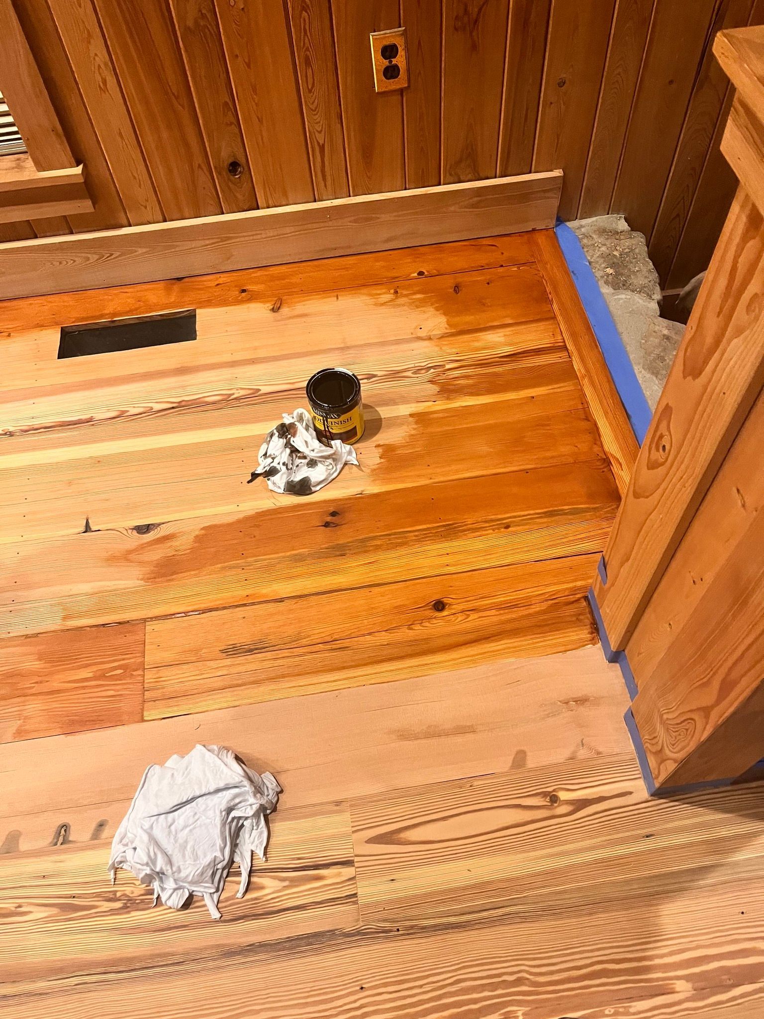 Wooden floor under construction, with a small spill, blue tape, and a paint can.