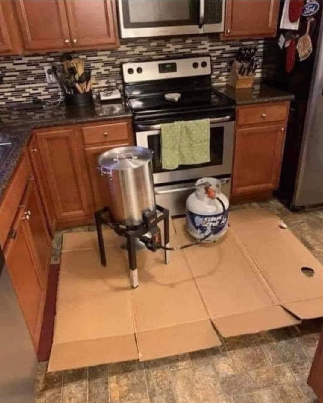 A kitchen with a pot and a propane tank on the floor.