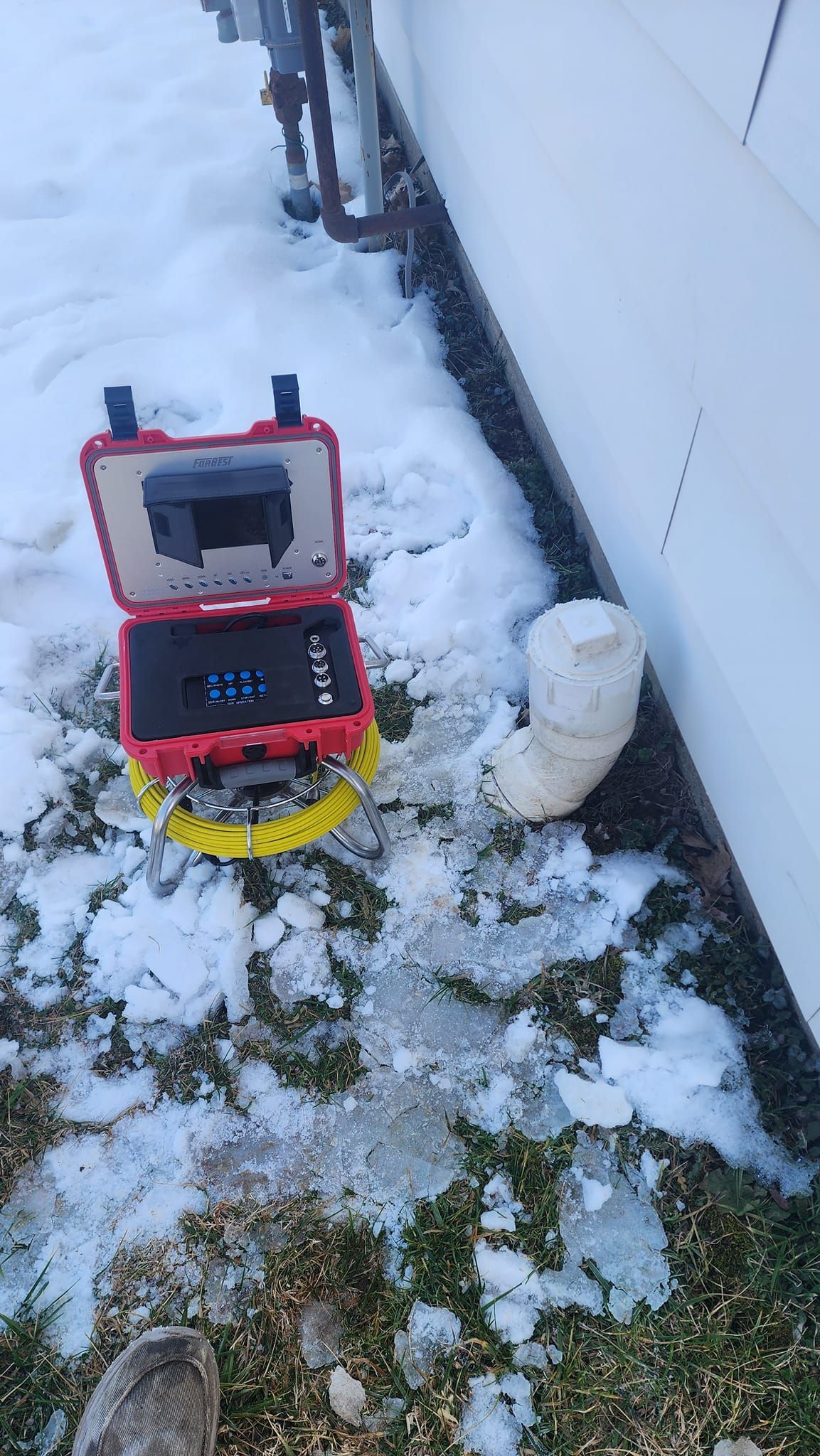A camera is sitting in the snow next to a pipe.