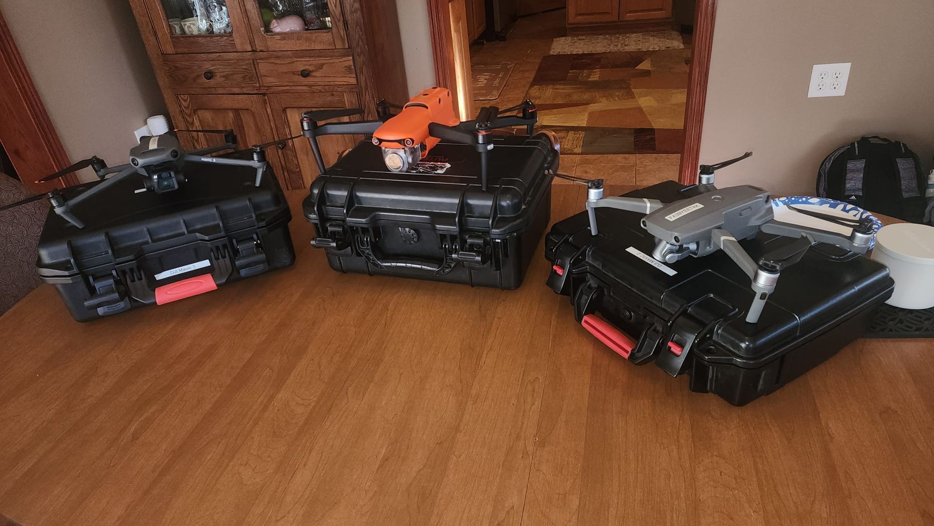 Three drones are sitting on top of hard cases on a wooden floor.