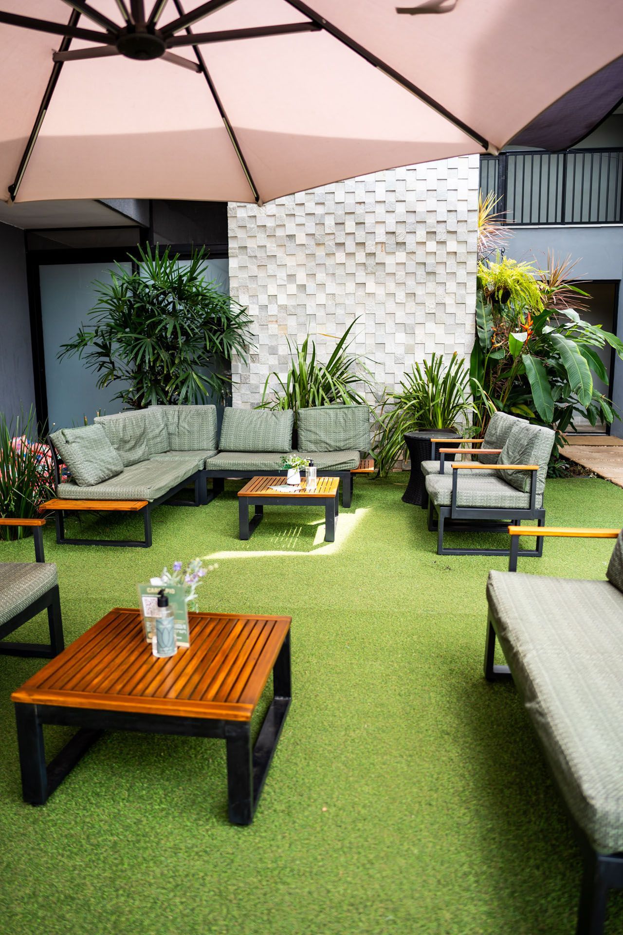 Área de estar externa com grama verde, móveis de madeira e um grande guarda-sol.