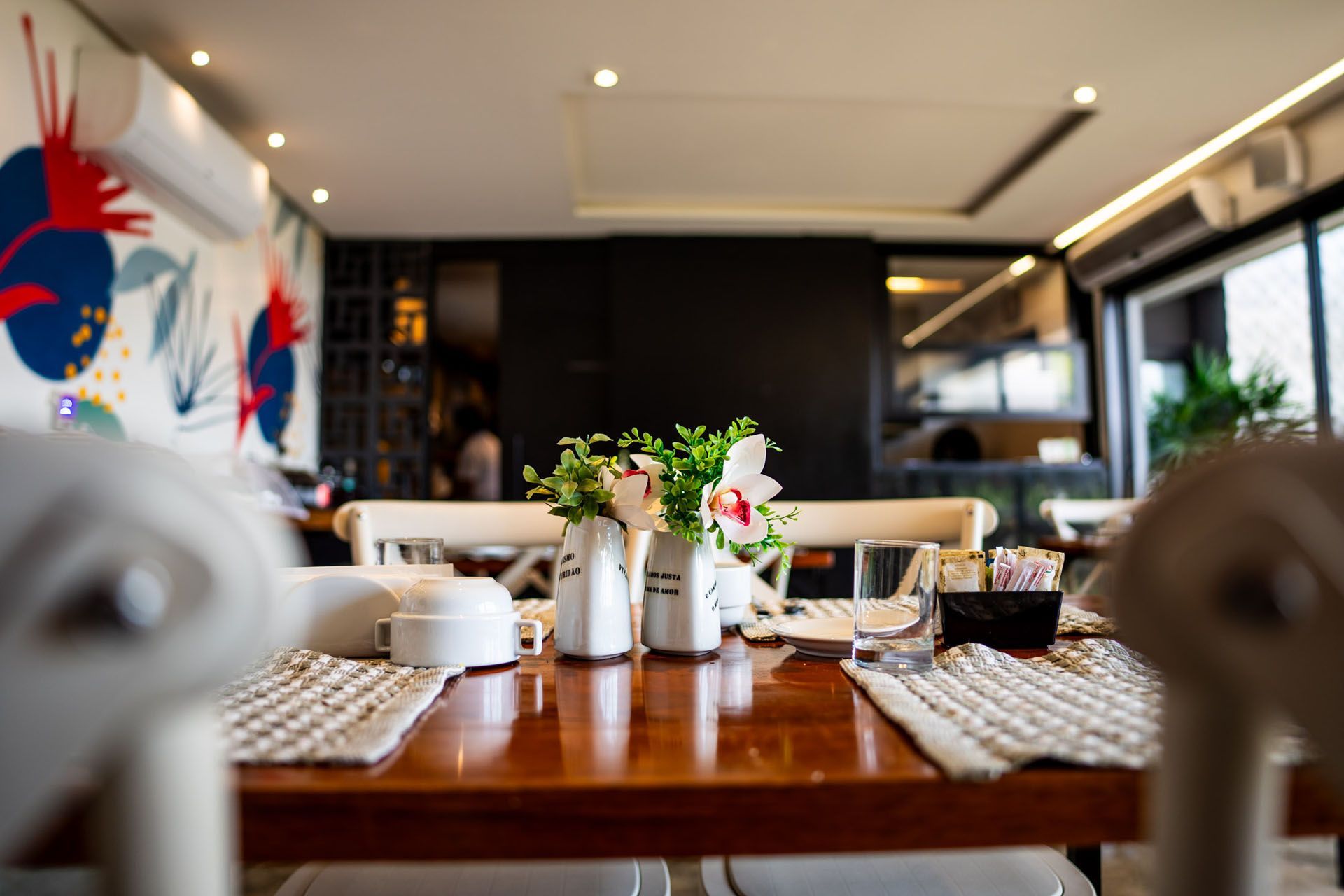 Mesa de restaurante com vaso de flores, saleiro e pimenteiro e jogos americanos; interior.