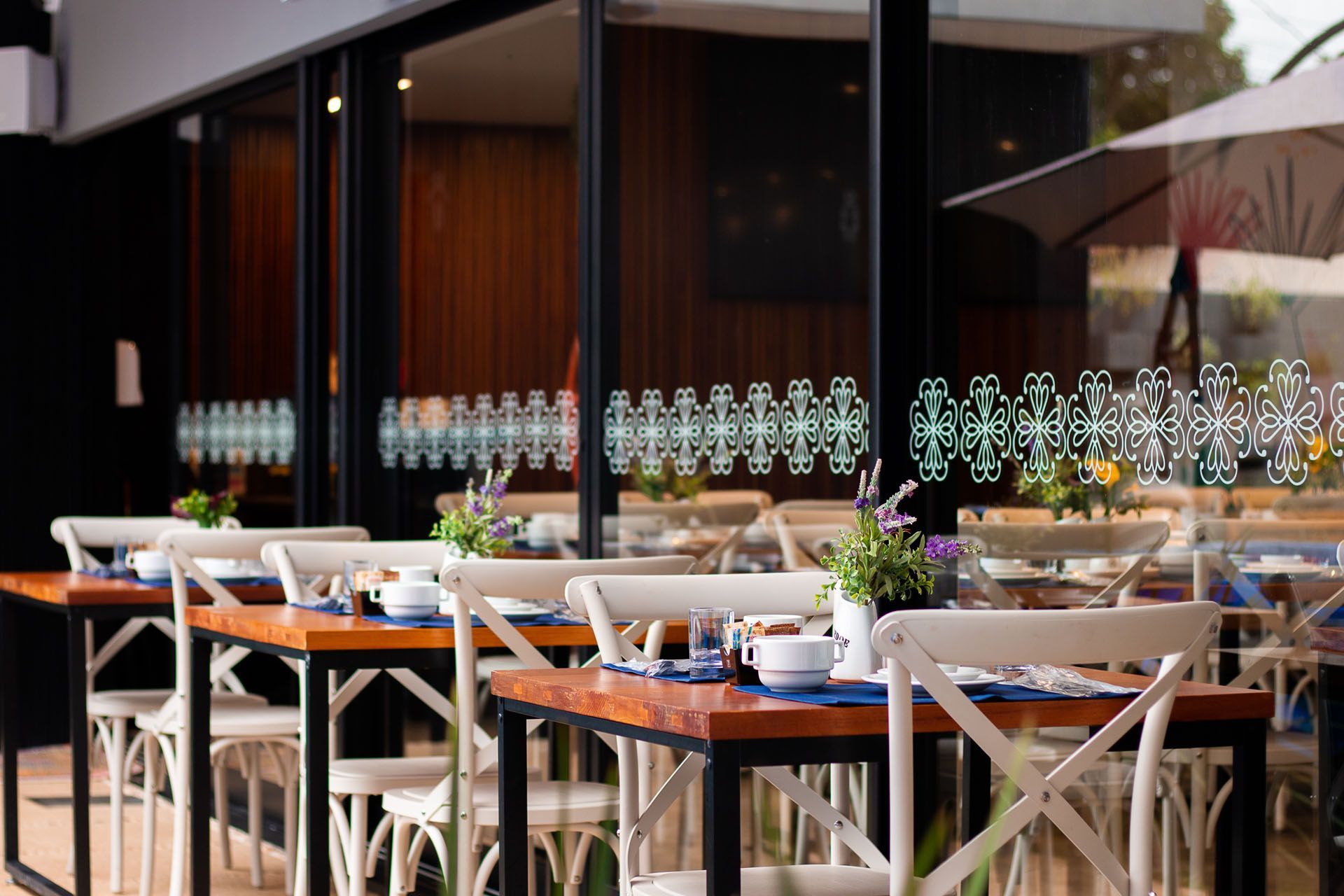 Mesas de restaurante com cadeiras brancas, vistas através de uma janela com padrões decorativos.