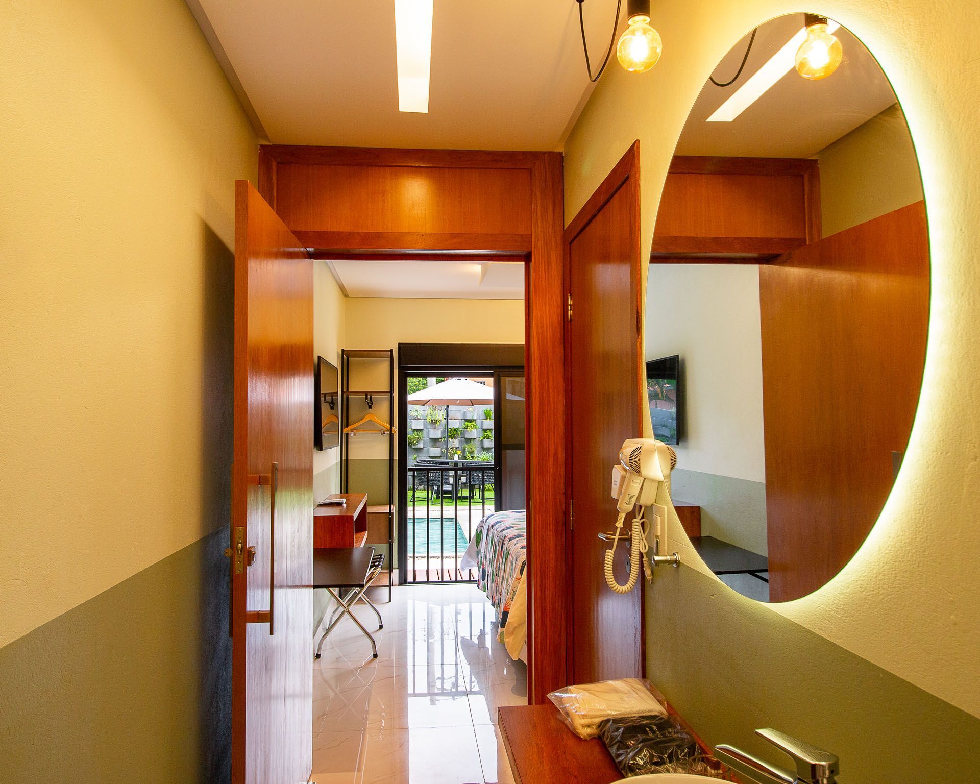 Corredor com espelho e portas abertas que dão acesso a um quarto com vista para a piscina externa.