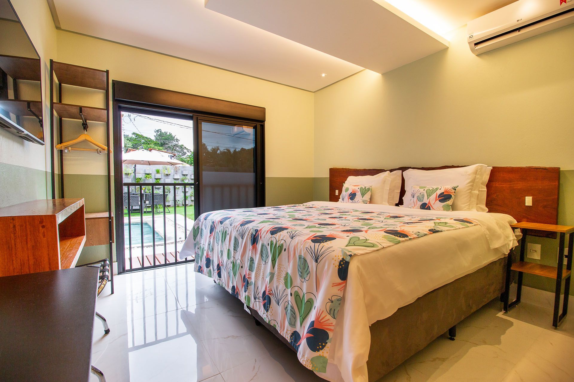 Quarto com cama de casal, porta de vidro deslizante e vista parcial para a piscina externa.
