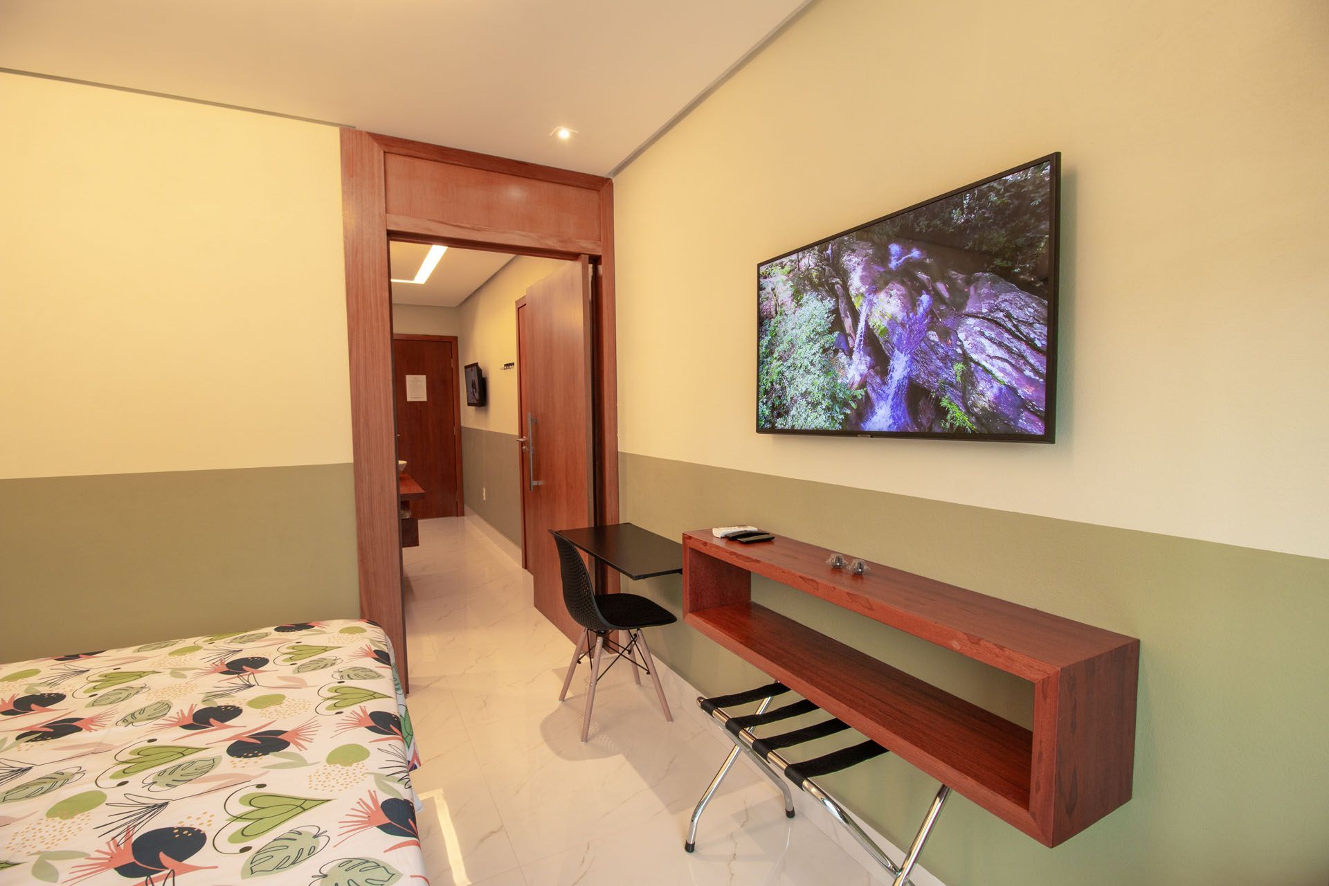 Um quarto de hotel com cama, TV, escrivaninha e uma porta que dá para outro quarto.