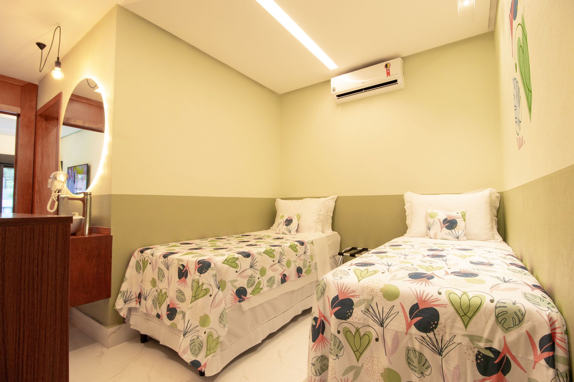 Dois beliches em um quarto com paredes verde-claras. Colchas florais e um espelho na parede.