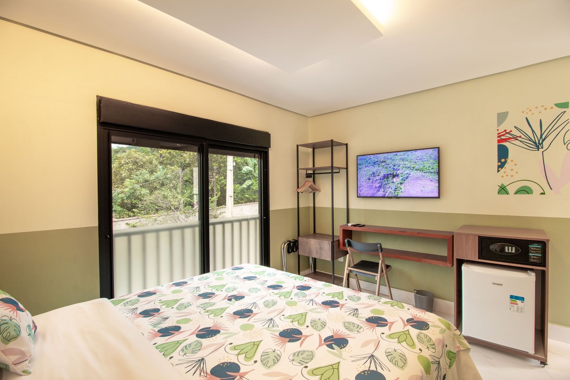 Quarto de hotel com duas camas de solteiro, TV, escrivaninha e varanda.