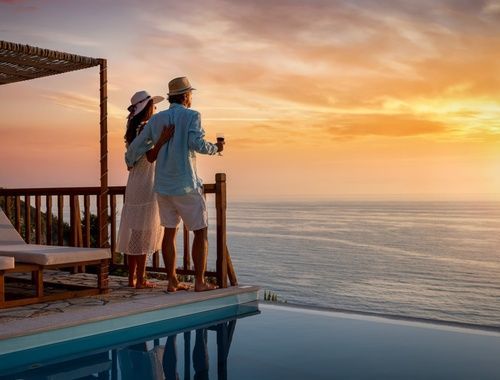 A man and a woman are standing on a balcony overlooking the ocean.