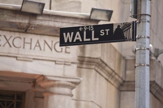 A wall street sign is hanging on a pole in front of a building