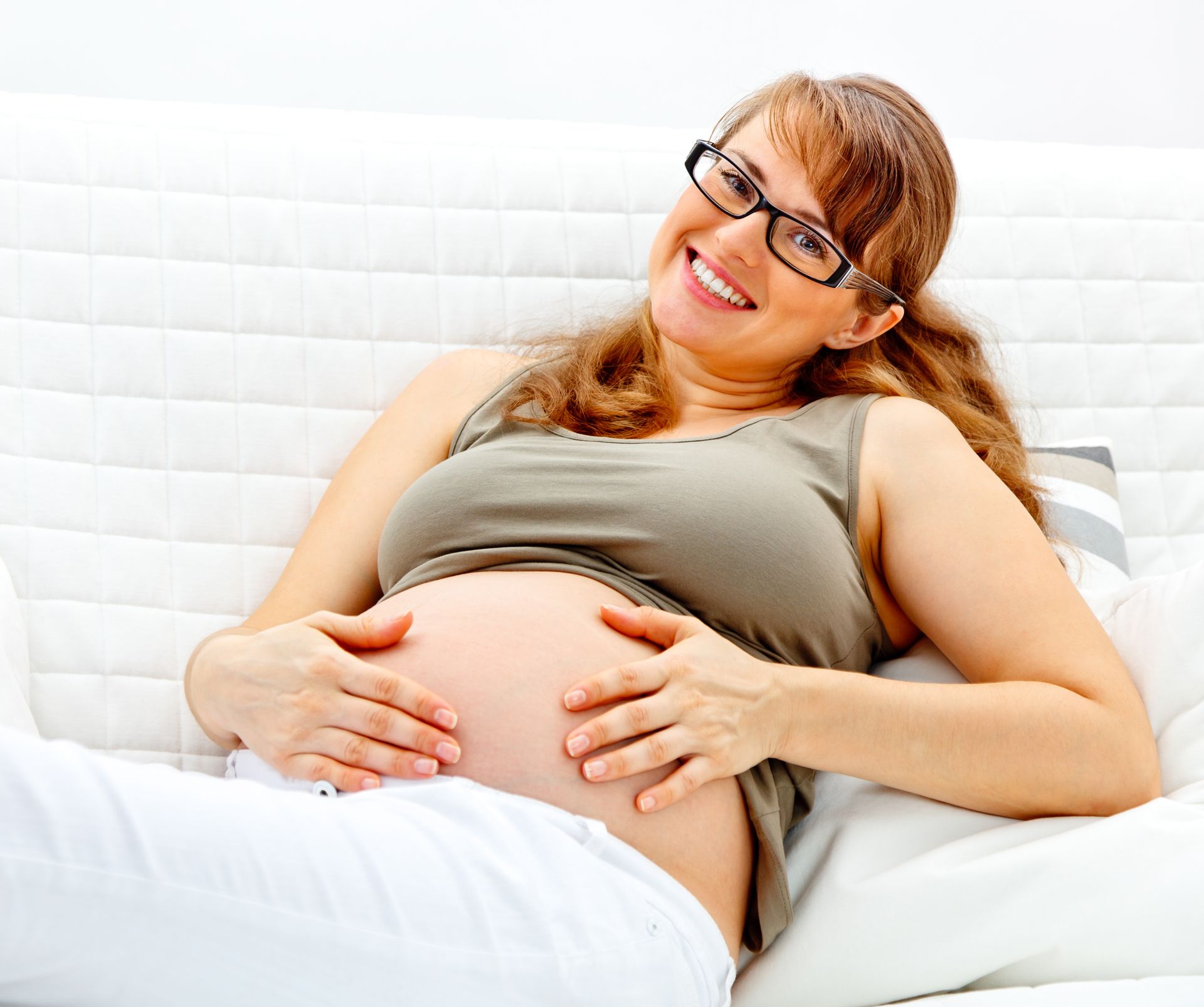 A pregnant woman wearing glasses is laying on a couch