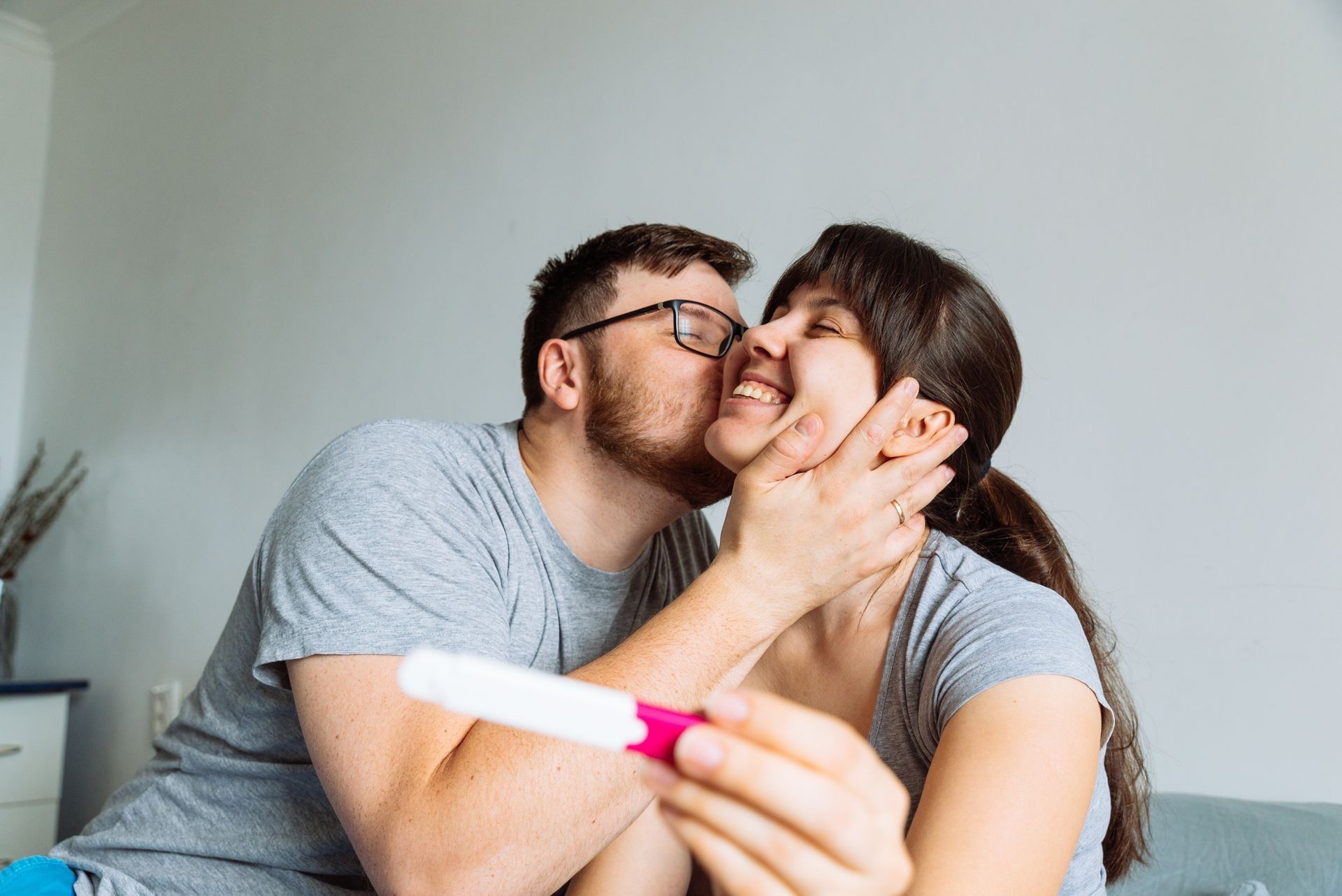 A man is kissing a woman on the cheek while holding a pregnancy test.