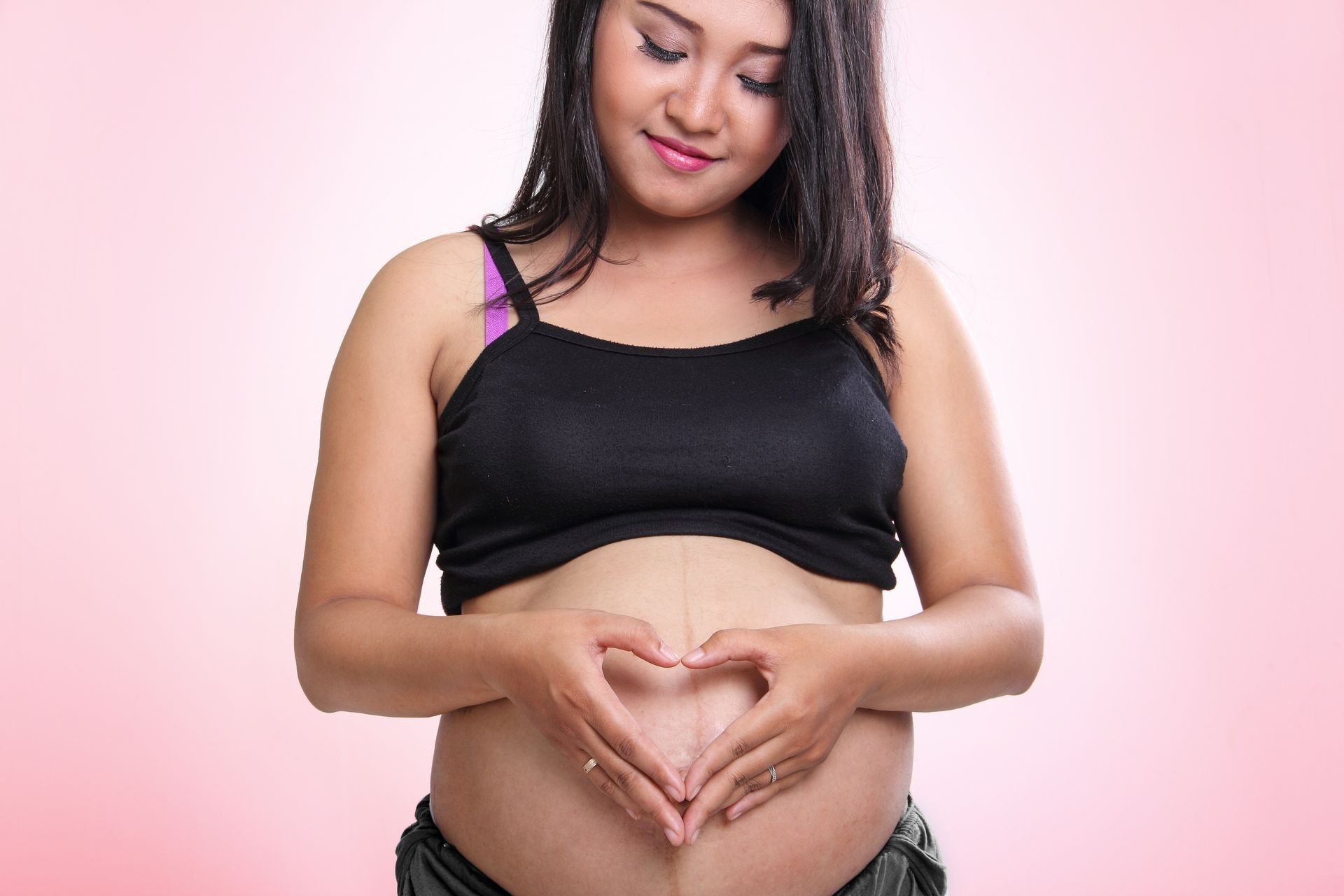 A pregnant woman is making a heart shape with her hands on her belly.