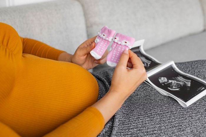 A pregnant woman is holding a pair of pink baby socks and looking at an ultrasound.