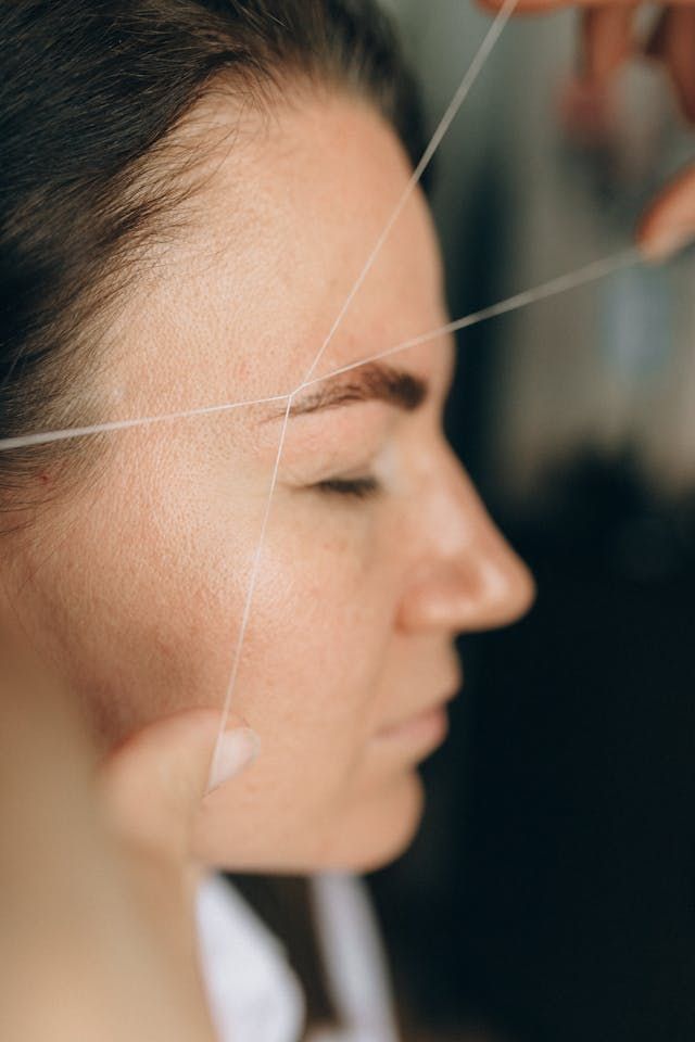 Une femme se fait épiler les sourcils au fil dans un salon de beauté.
