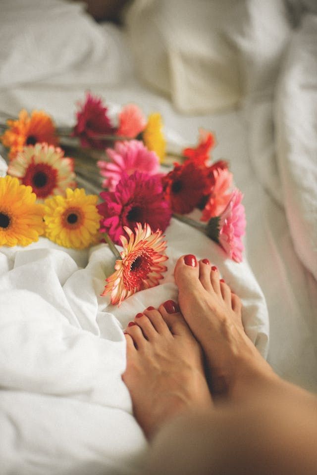 Les pieds d'une femme sont posés sur un lit avec des fleurs.