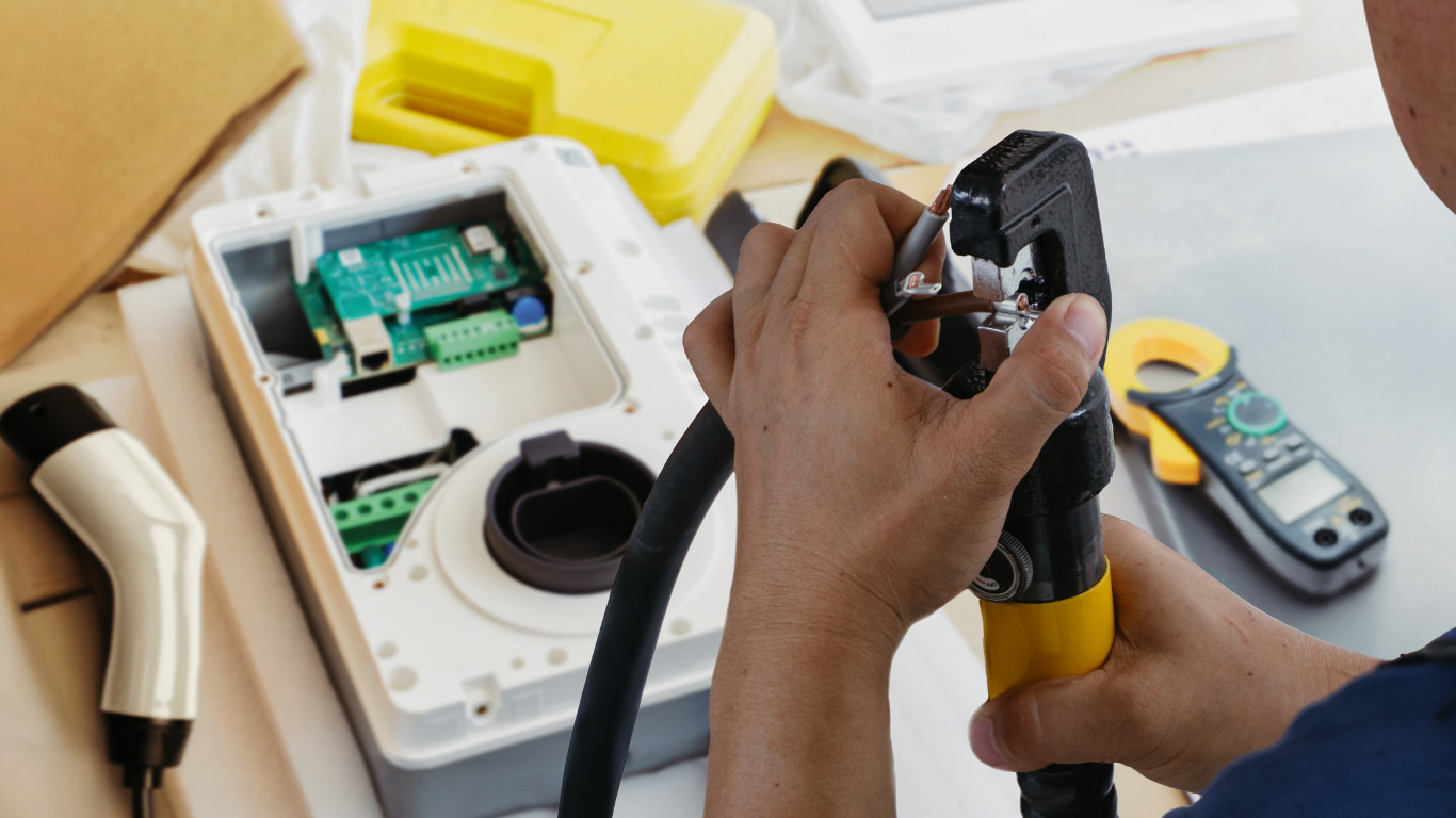Hands repairing a device with a screwdriver beside an open electronic unit and tools on a workbench