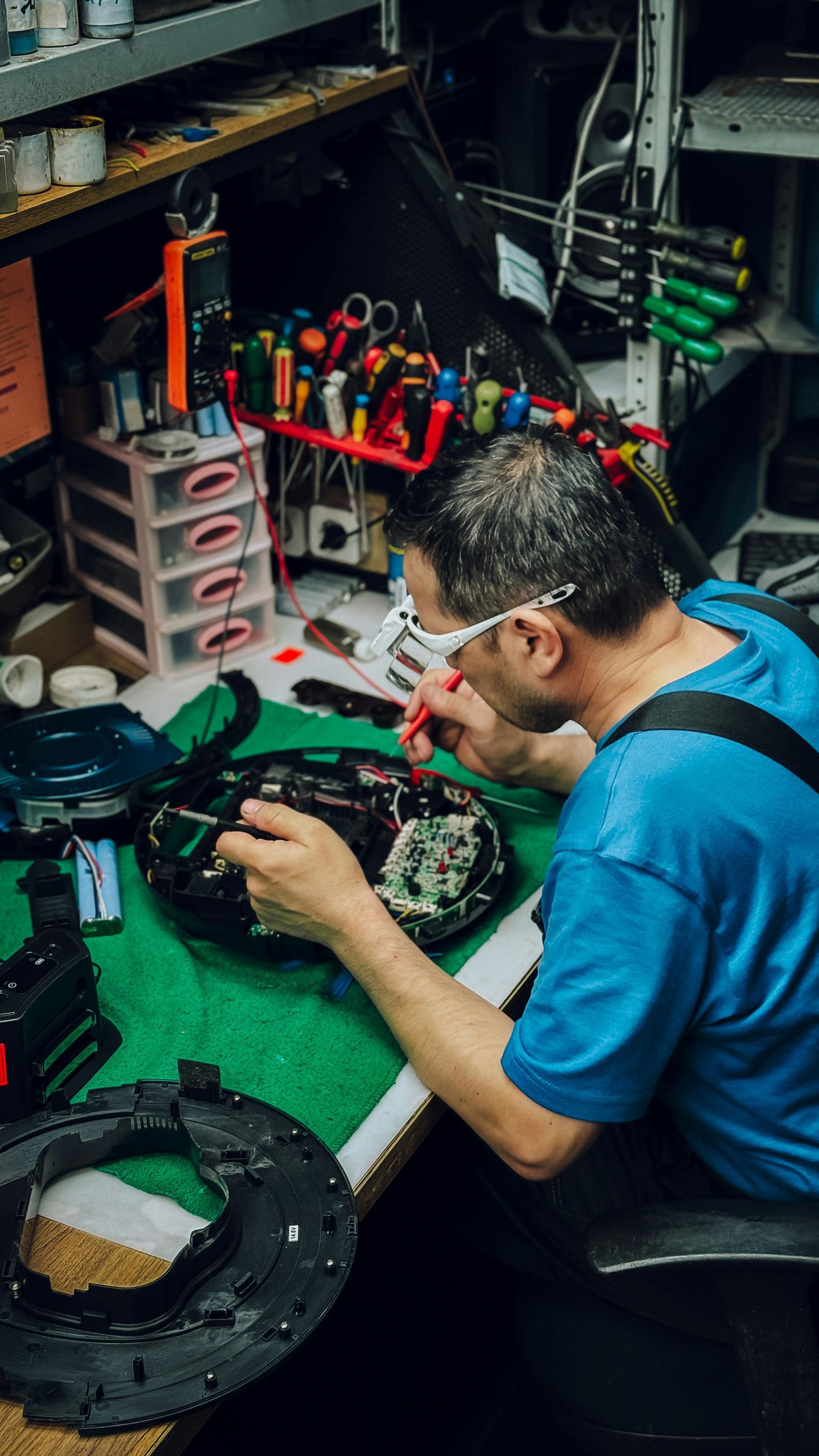 Mechanic in blue shirt repairing a watch at a cluttered workbench with tools and parts