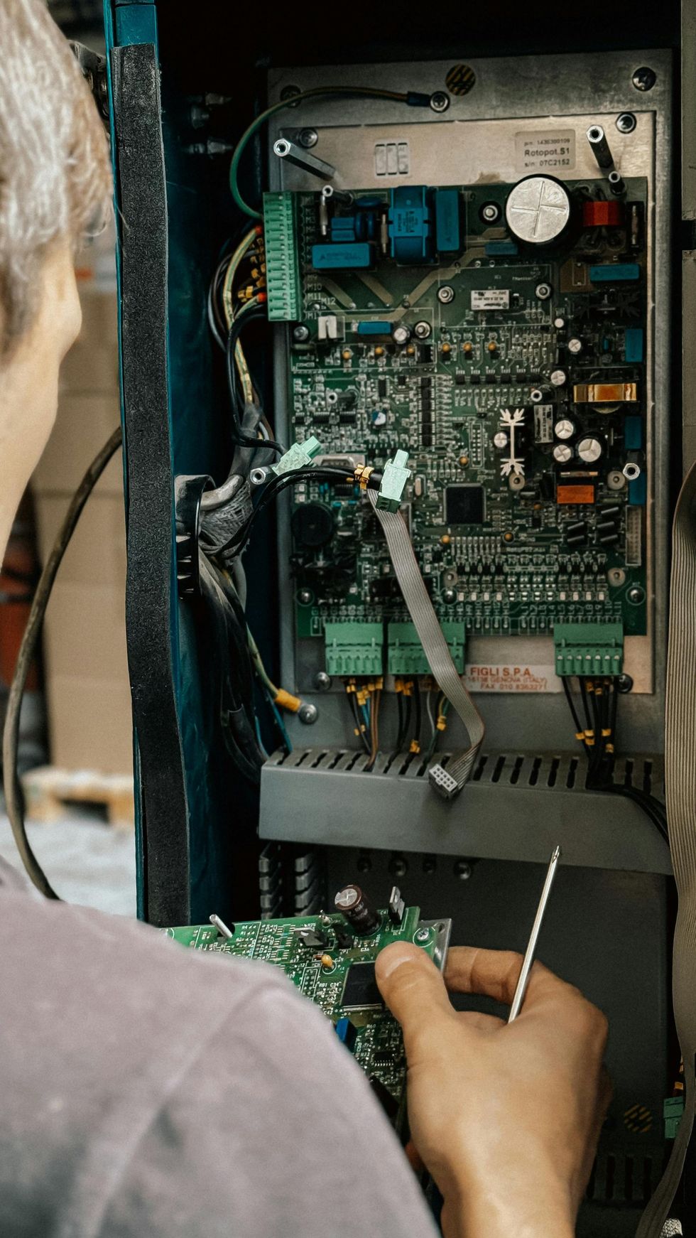 Technician repairing an open electrical control panel with circuit boards and wires.