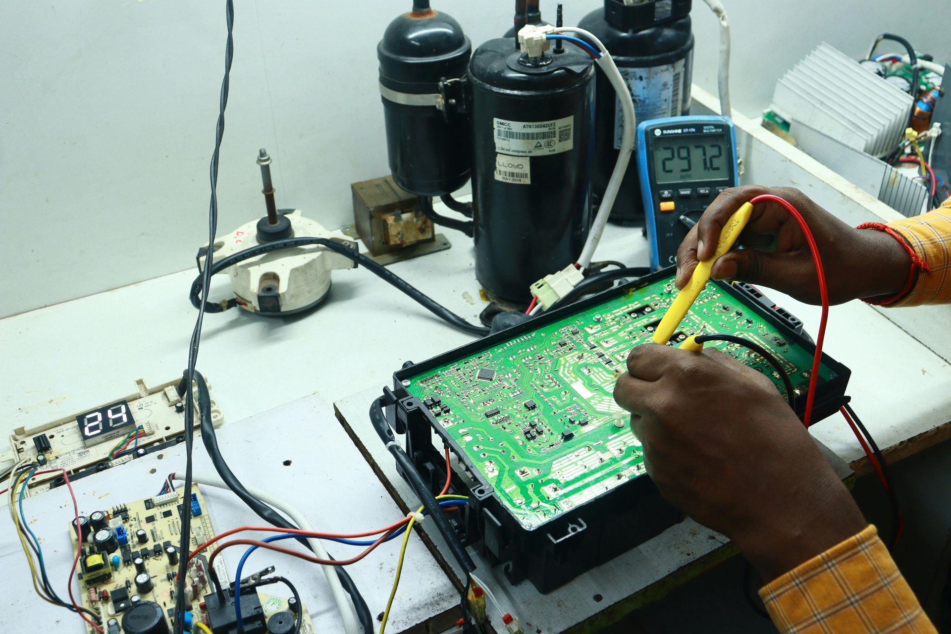 Technician testing a green circuit board on a workbench with probes and electronic equipment