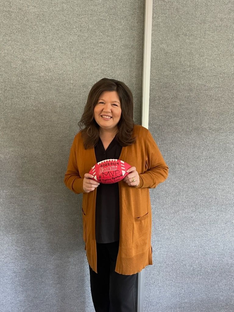 A woman in a brown cardigan is holding a red football.