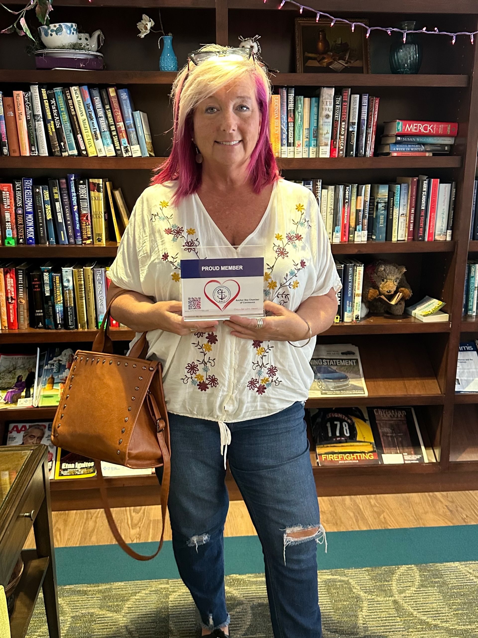 A woman with pink hair is holding a book in front of a bookshelf.