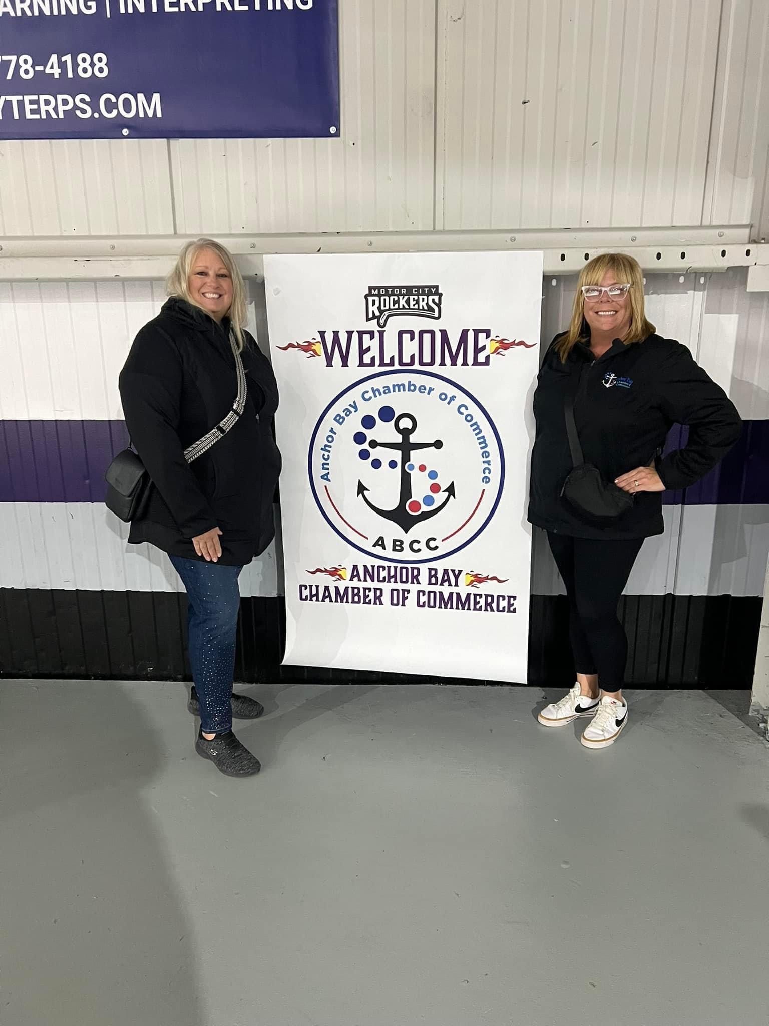 Two women are standing next to a welcome sign.