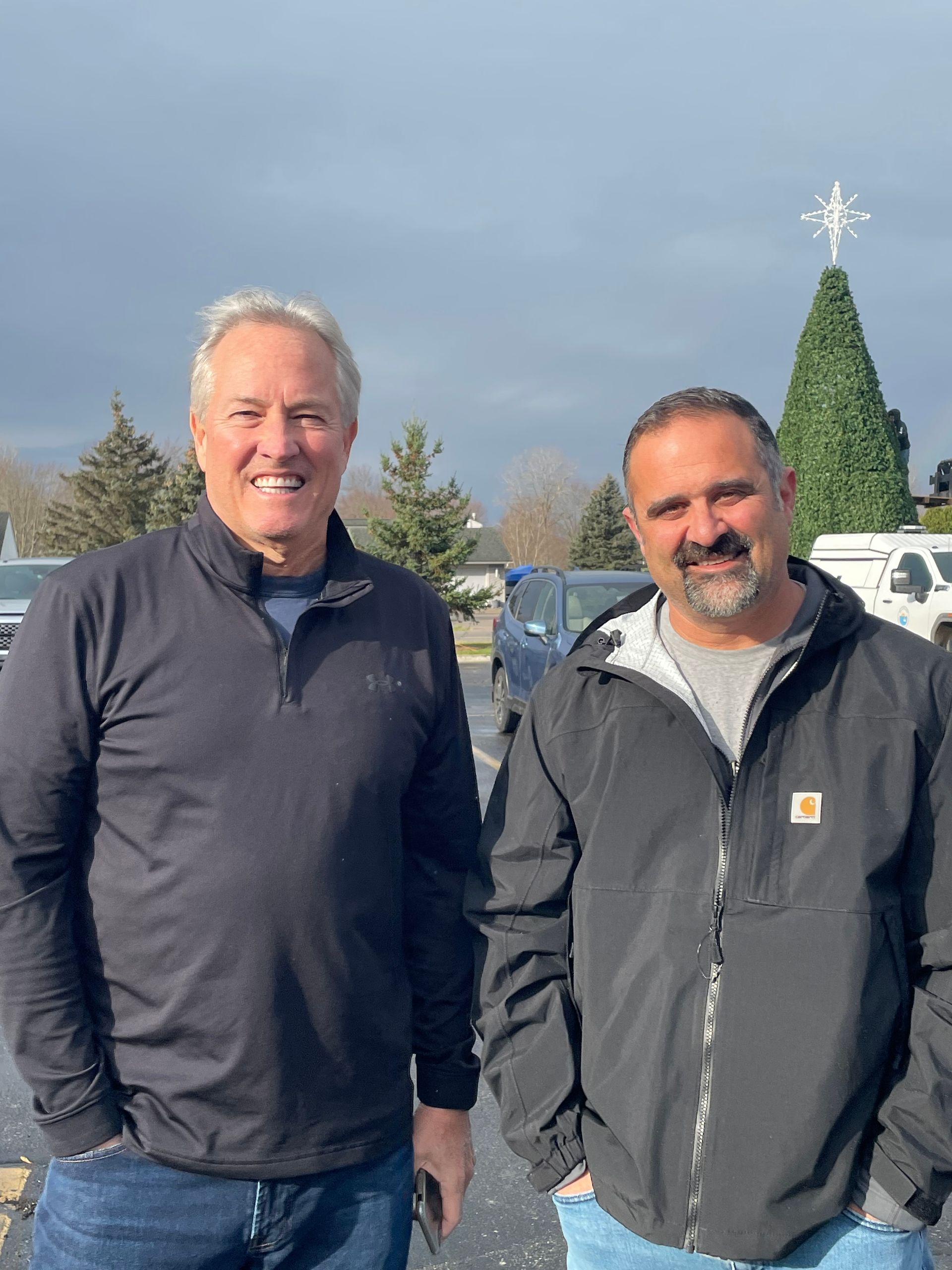 Two men are standing next to each other in front of a christmas tree.