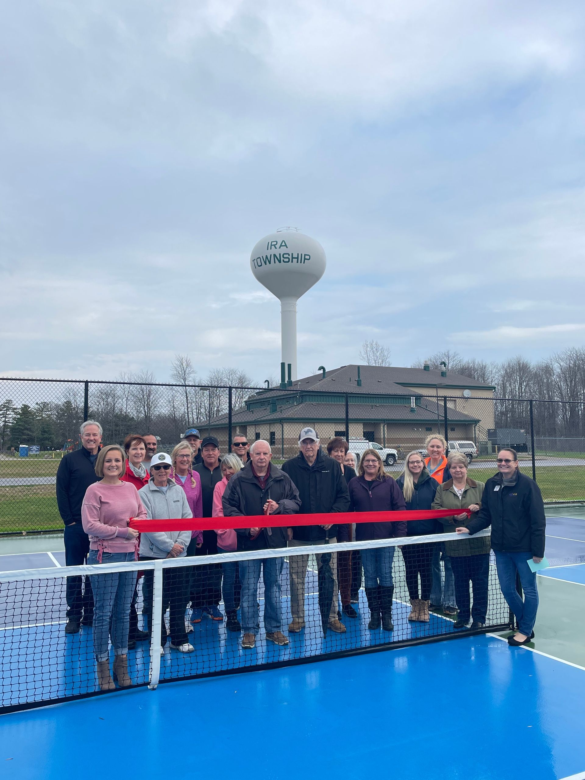 A group of people are cutting a red ribbon on a tennis court.
