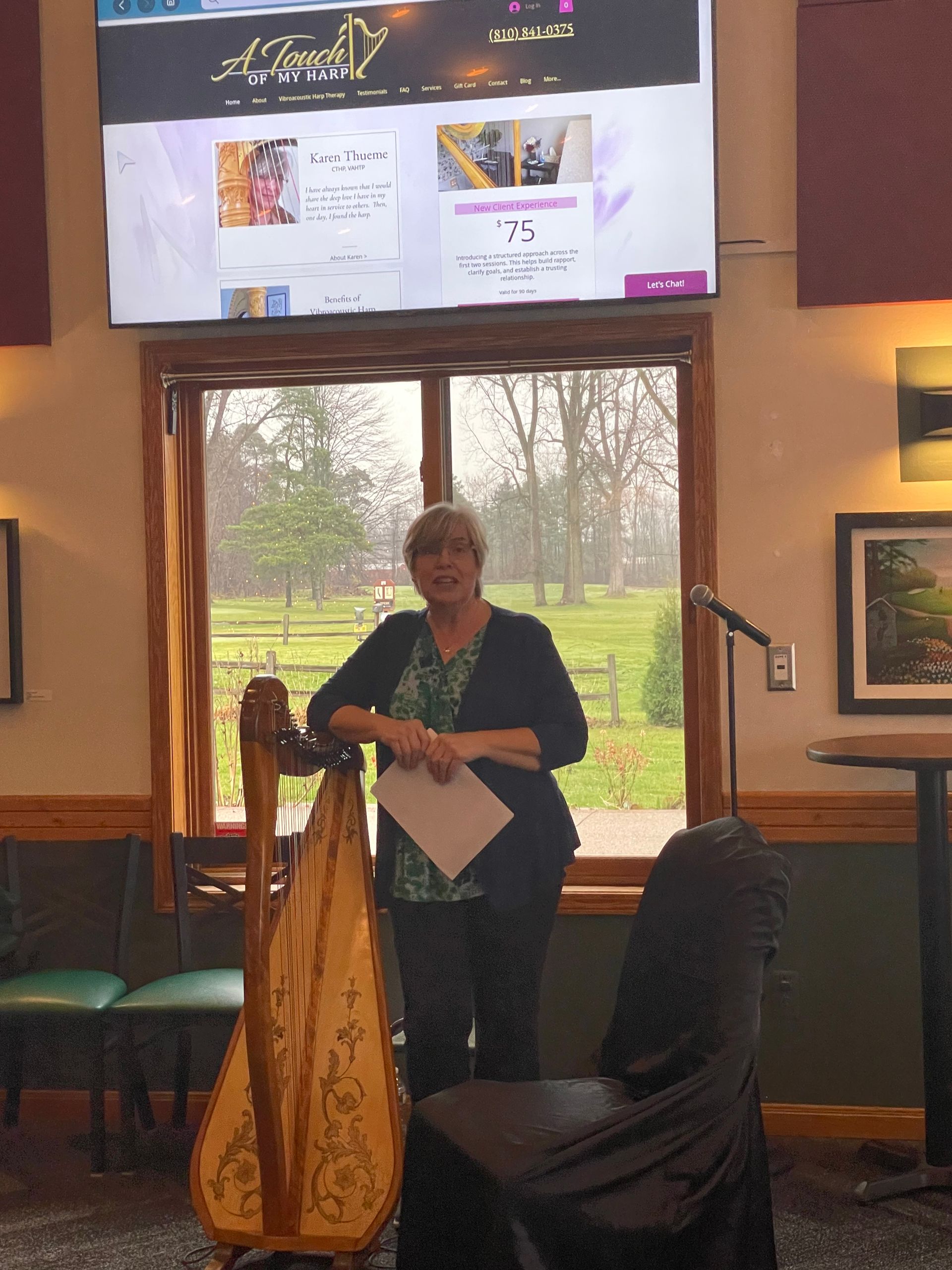 A woman playing a harp in front of a large screen.