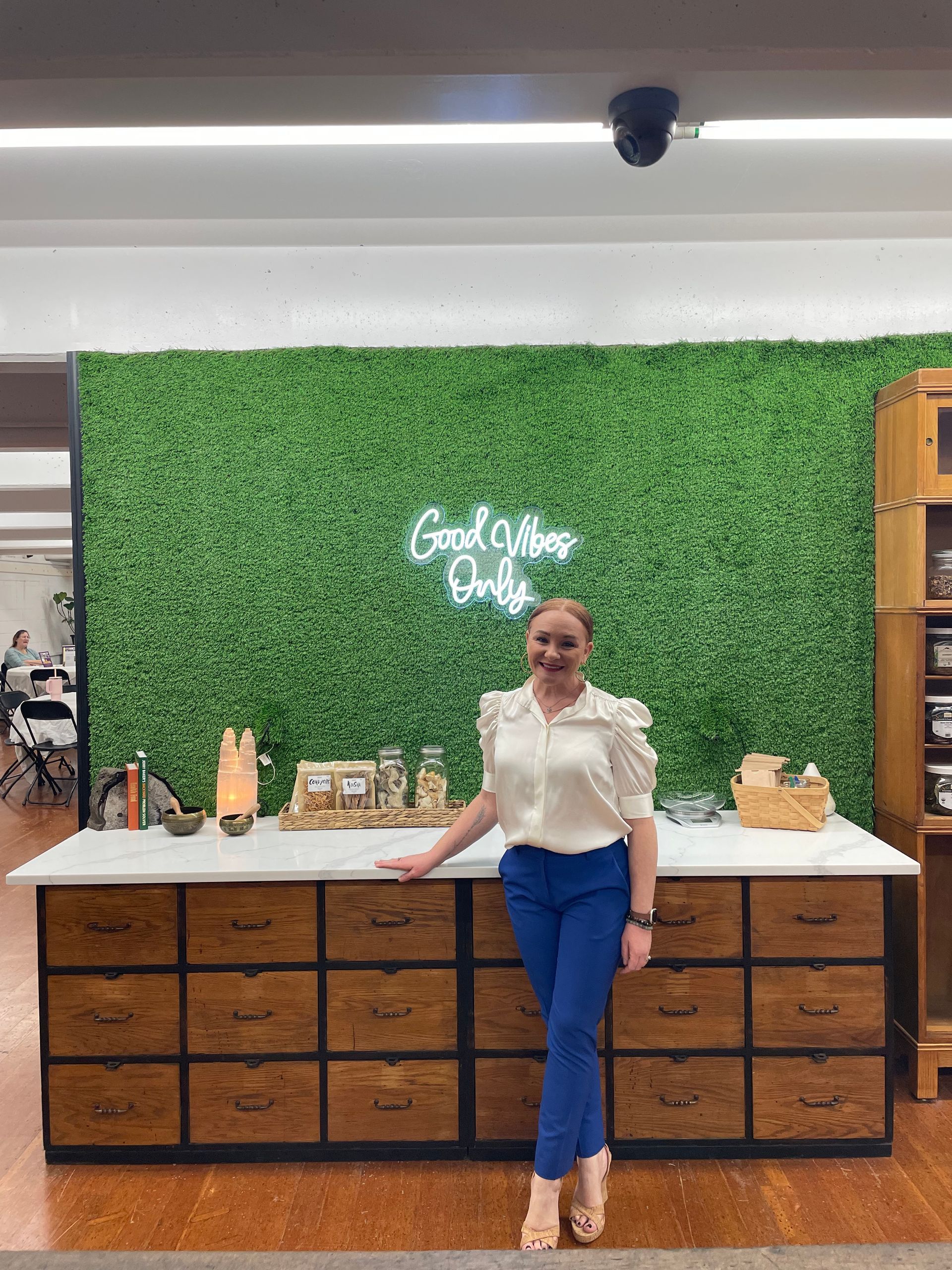 A woman is standing in front of a green wall with a neon sign that says `` good vibes only ''.