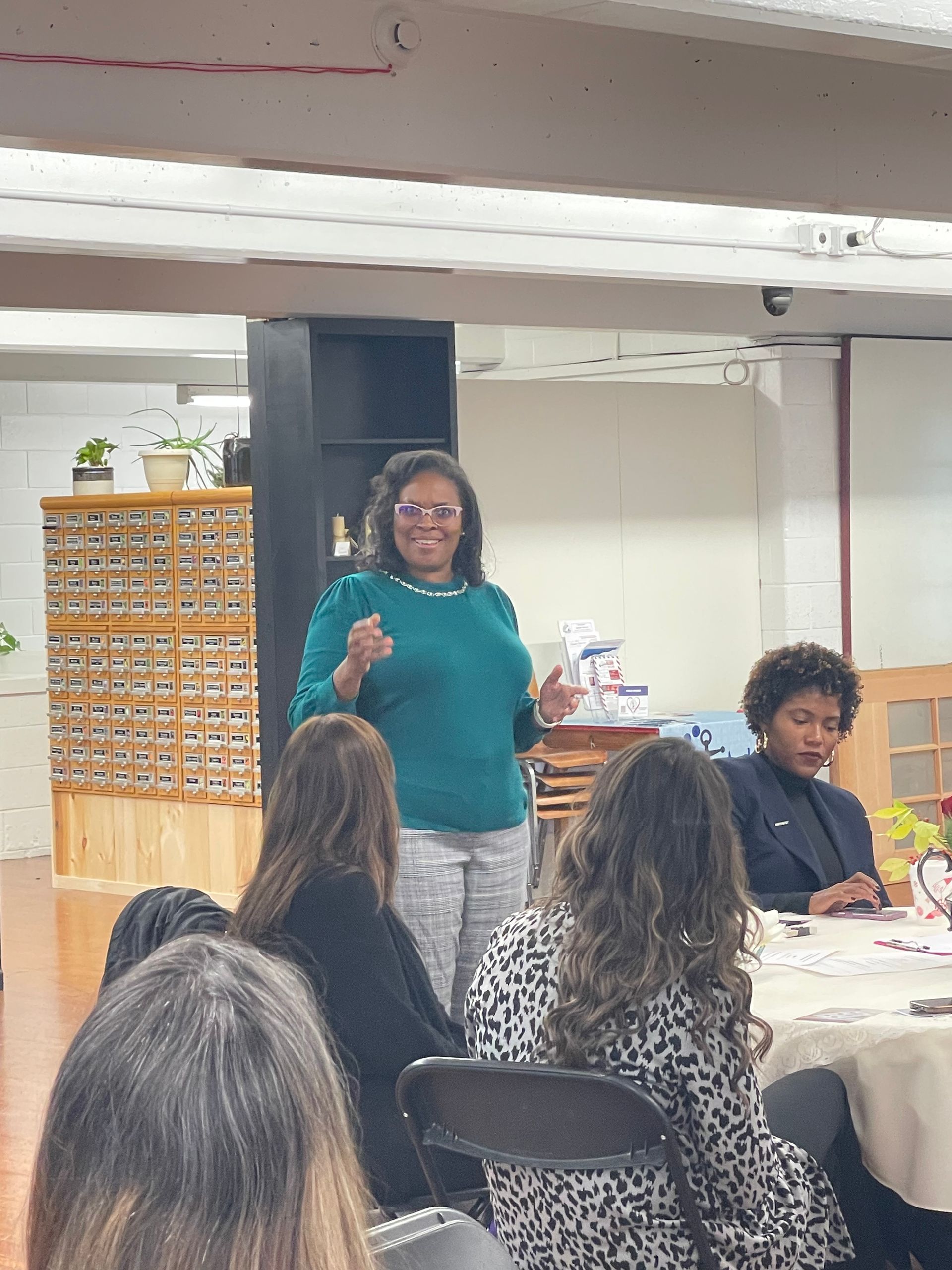 A woman is standing in front of a group of people sitting at tables.