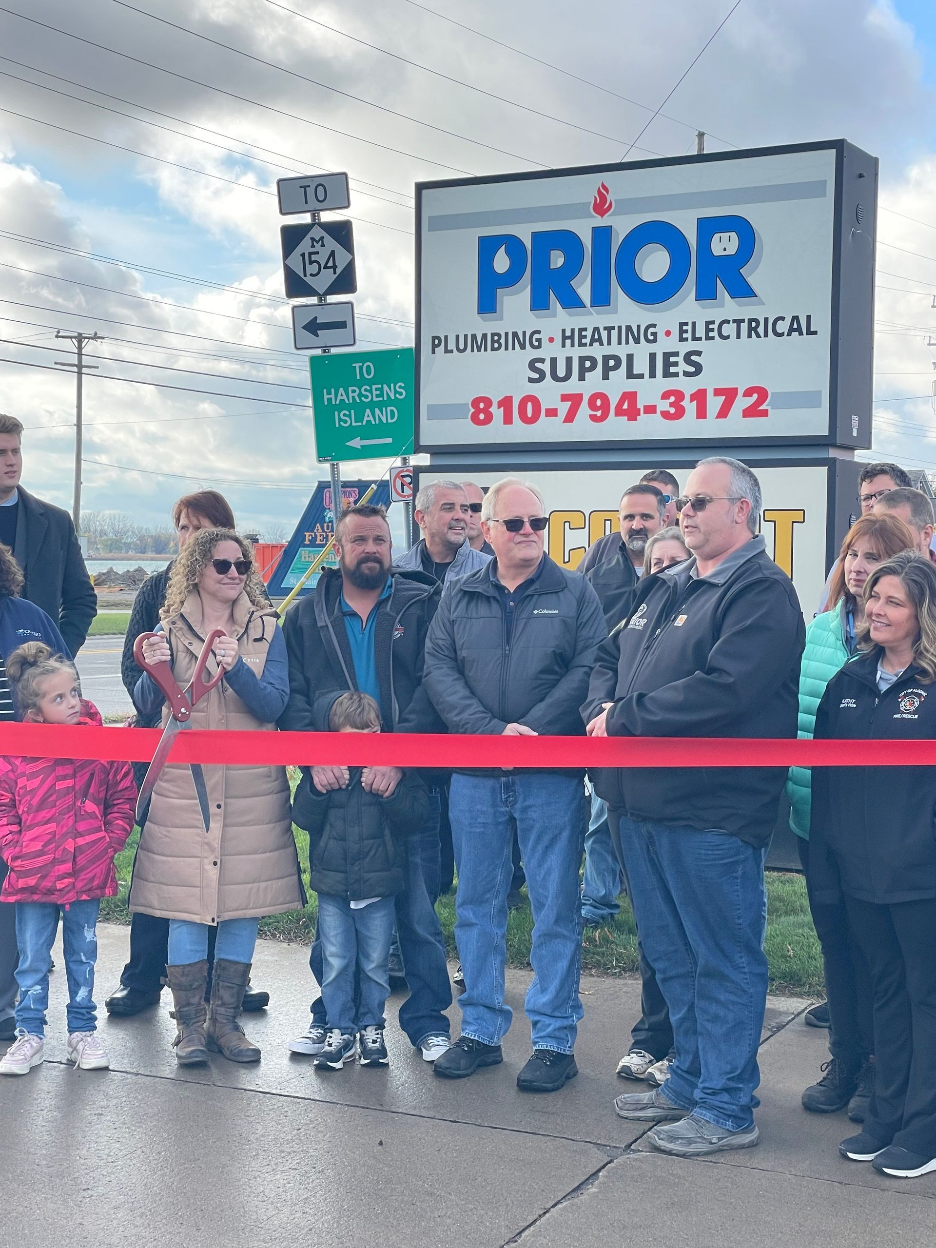 A group of people are standing in front of a prior plumbing heating electrical supplies sign.
