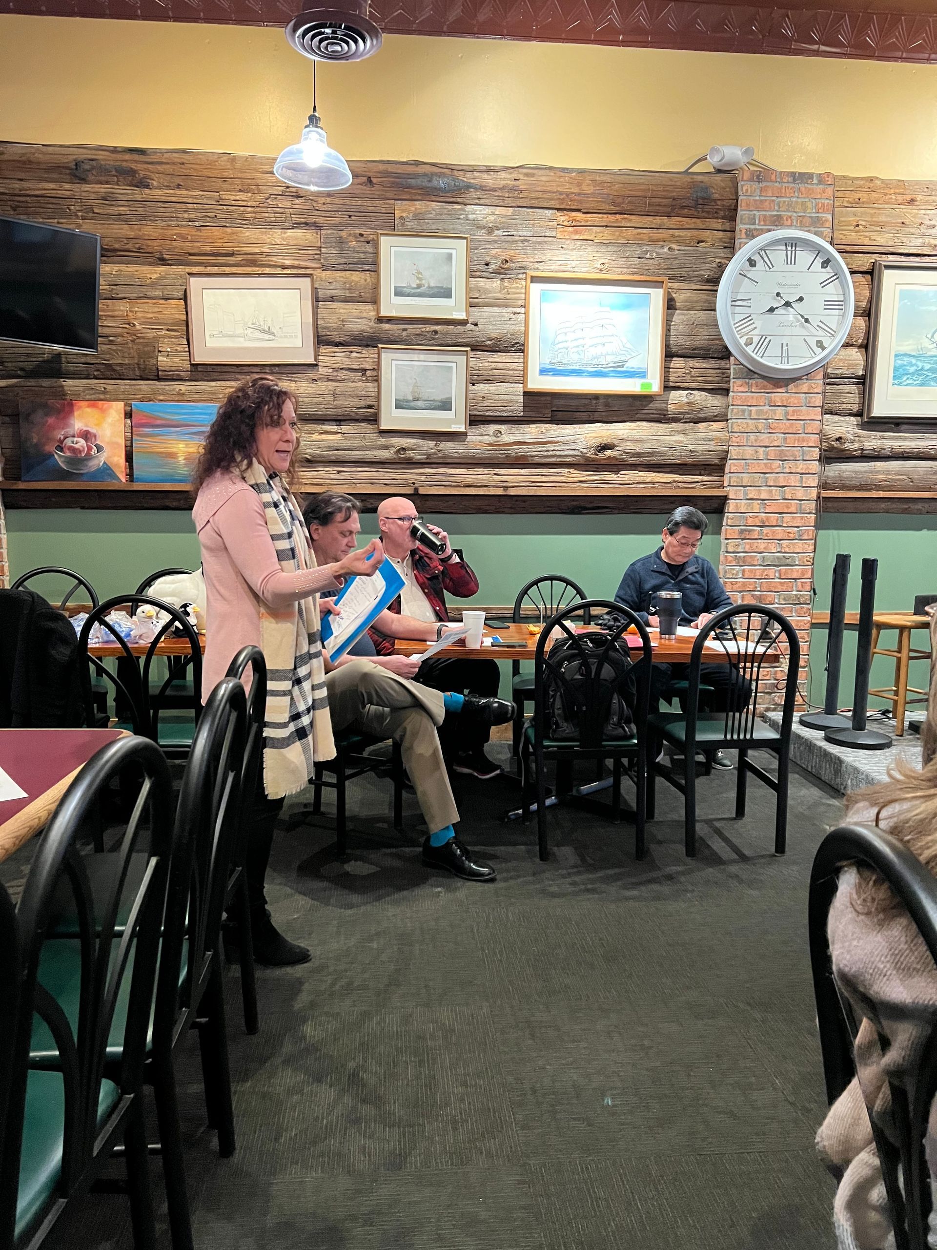 A group of people are sitting at tables in a restaurant with a clock on the wall