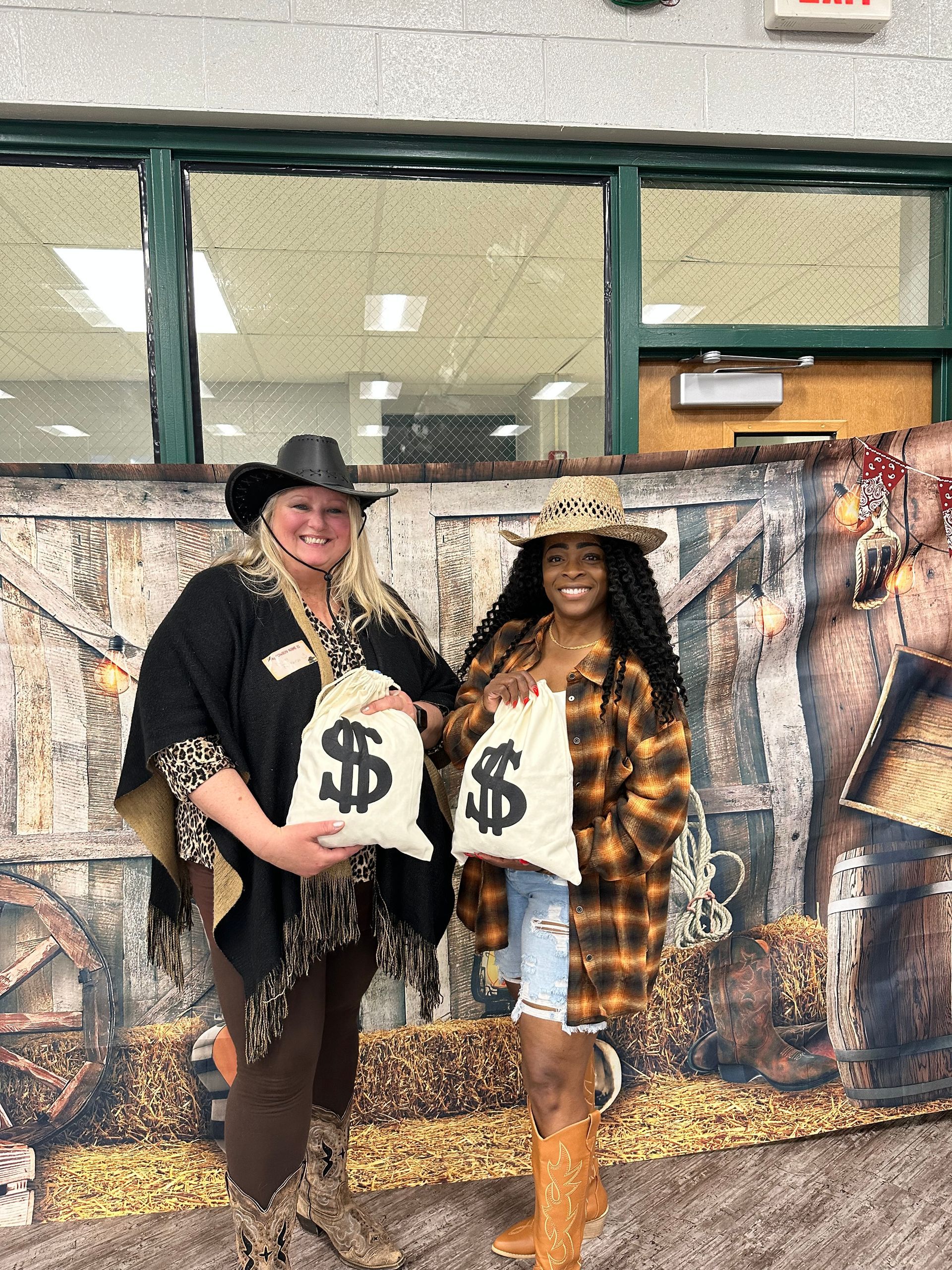 Two women in cowboy costumes are standing next to each other holding bags of money.