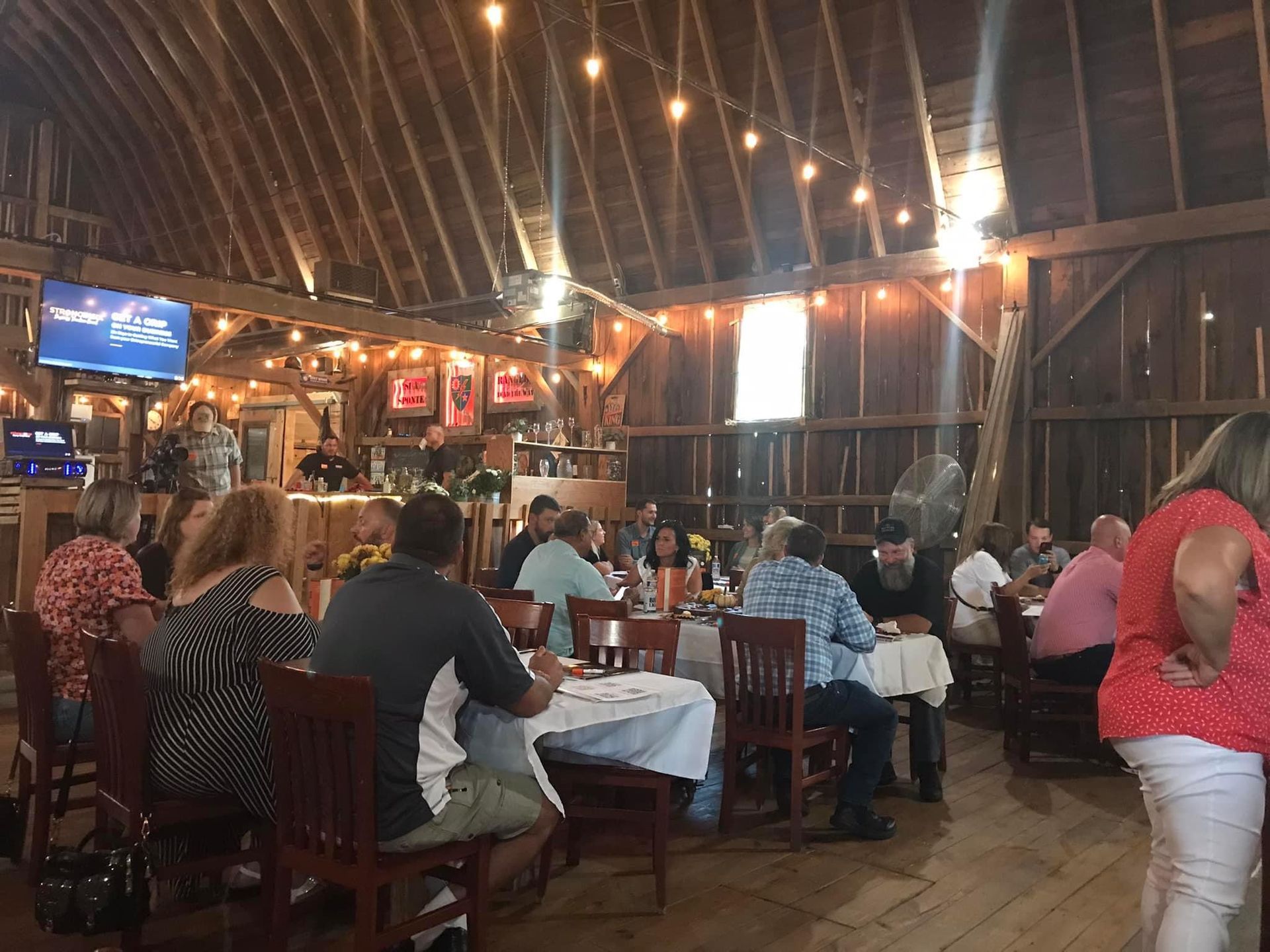A group of people are sitting at tables in a barn