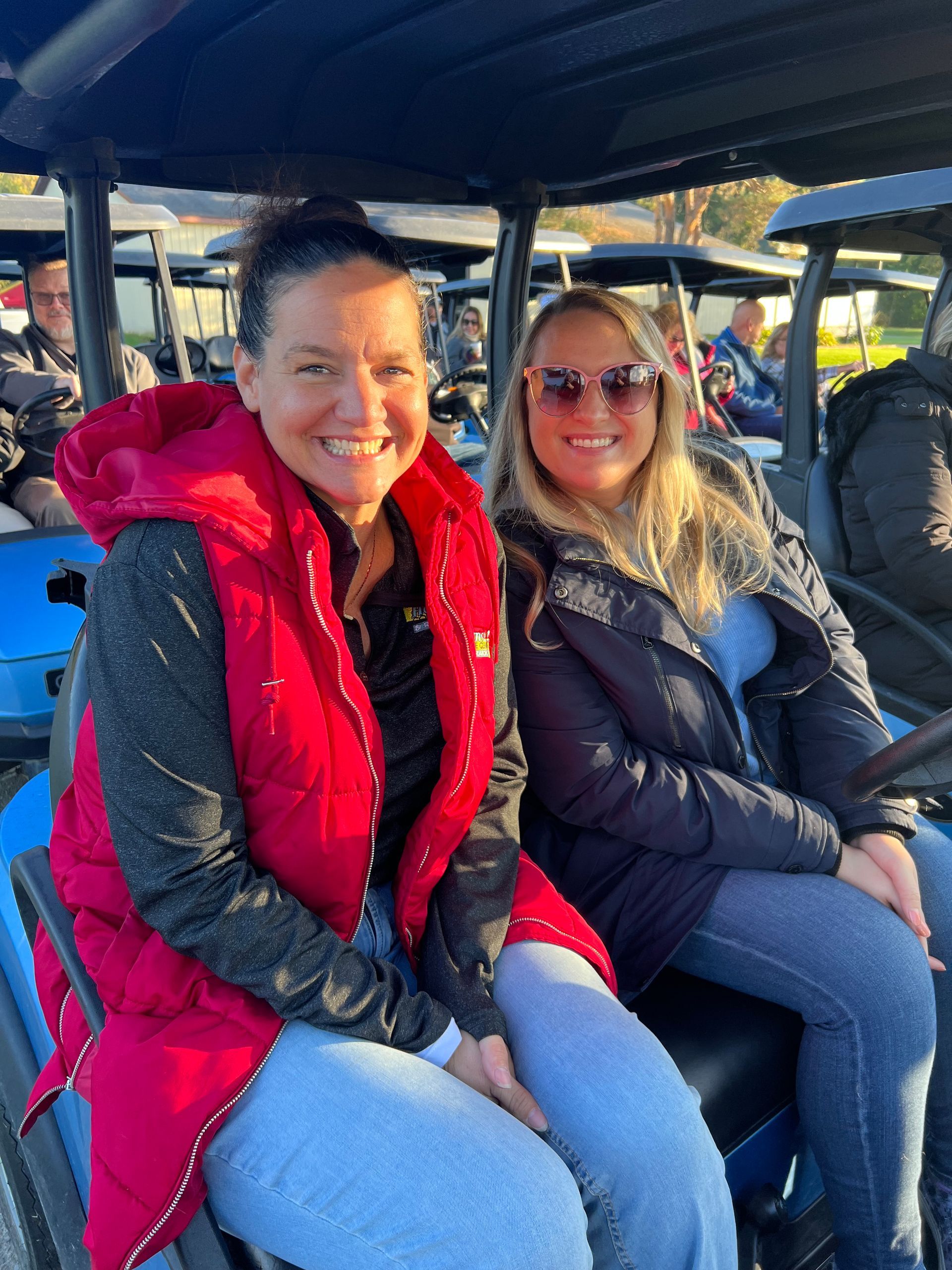 Two women are sitting in a golf cart and smiling for the camera