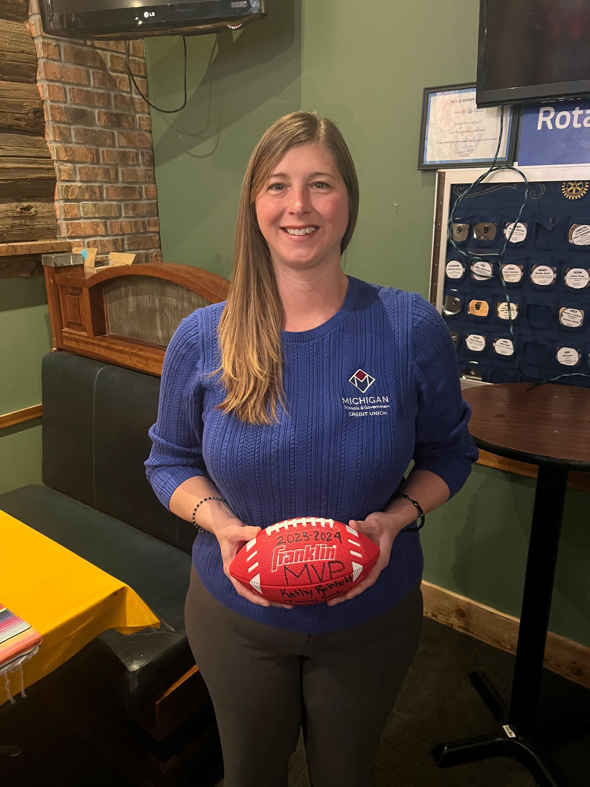 A woman in a blue sweater is holding a red football