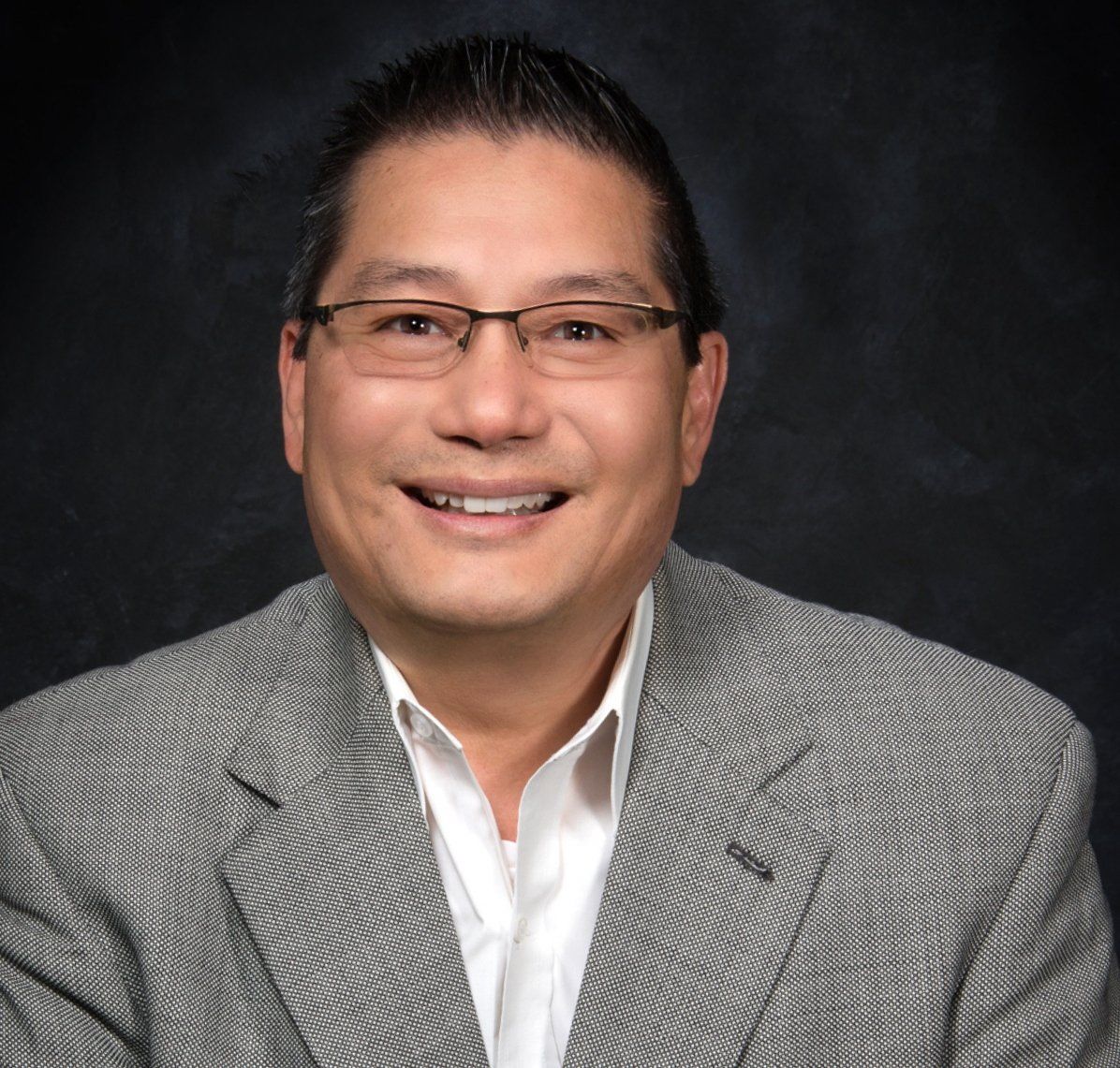 A man wearing glasses and a suit jacket smiles for the camera