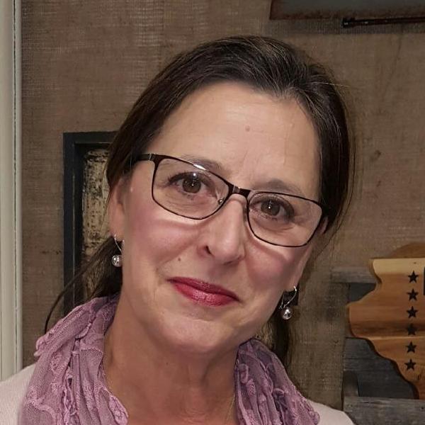 A woman wearing glasses and a purple scarf is looking at the camera.
