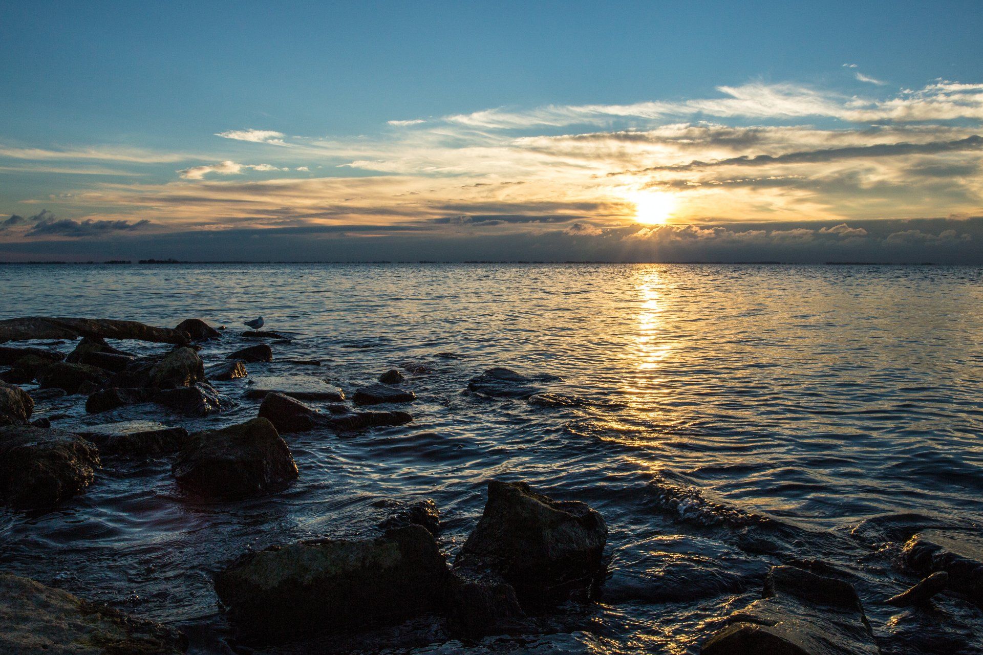 A sunset over a body of water with rocks in the foreground