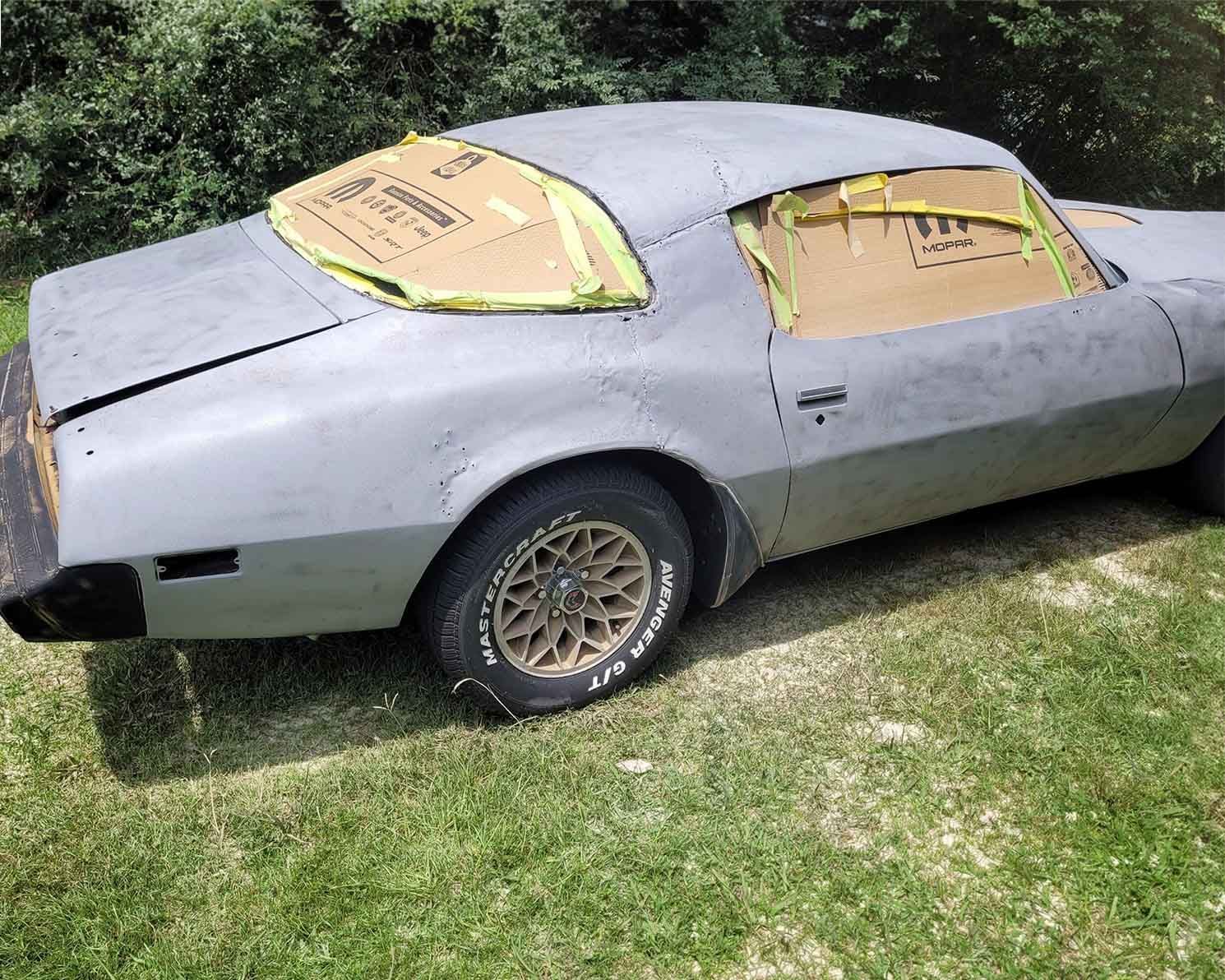 A gray car is parked in a grassy area and is being painted.