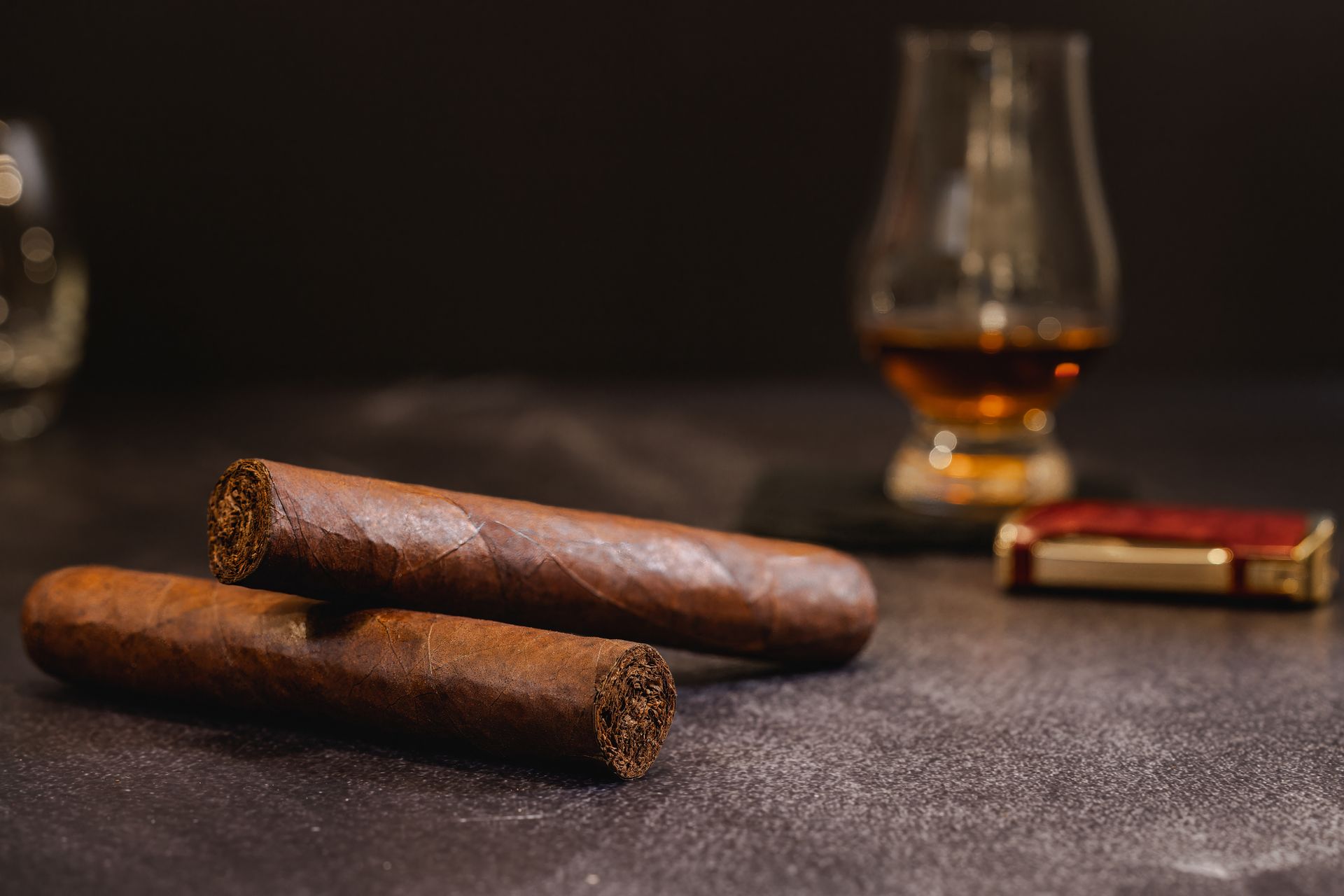 Two cigars are sitting on a table next to a glass of whiskey.