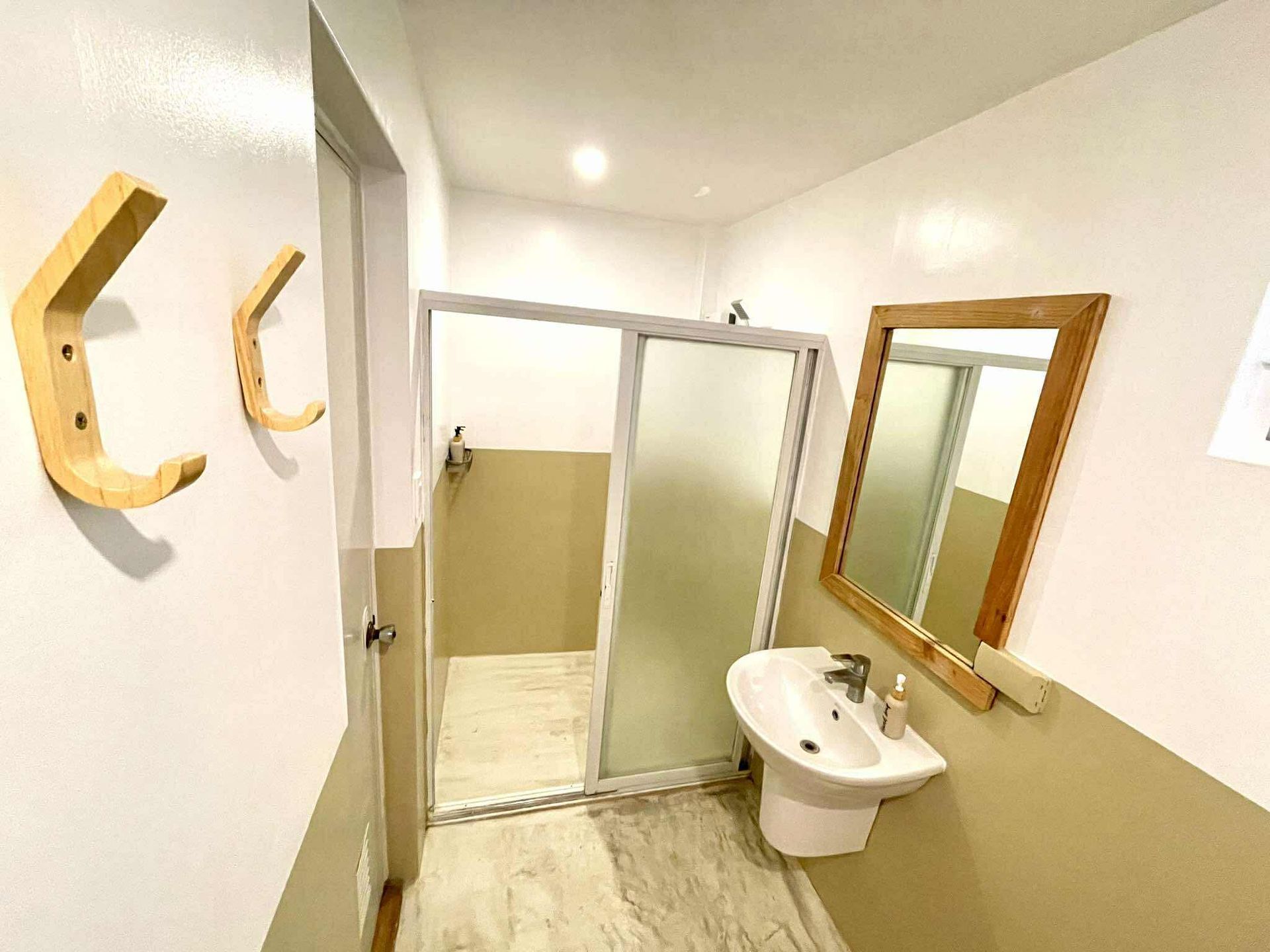 Bathroom with shower, sink, and mirror. White and tan walls with wooden hooks.