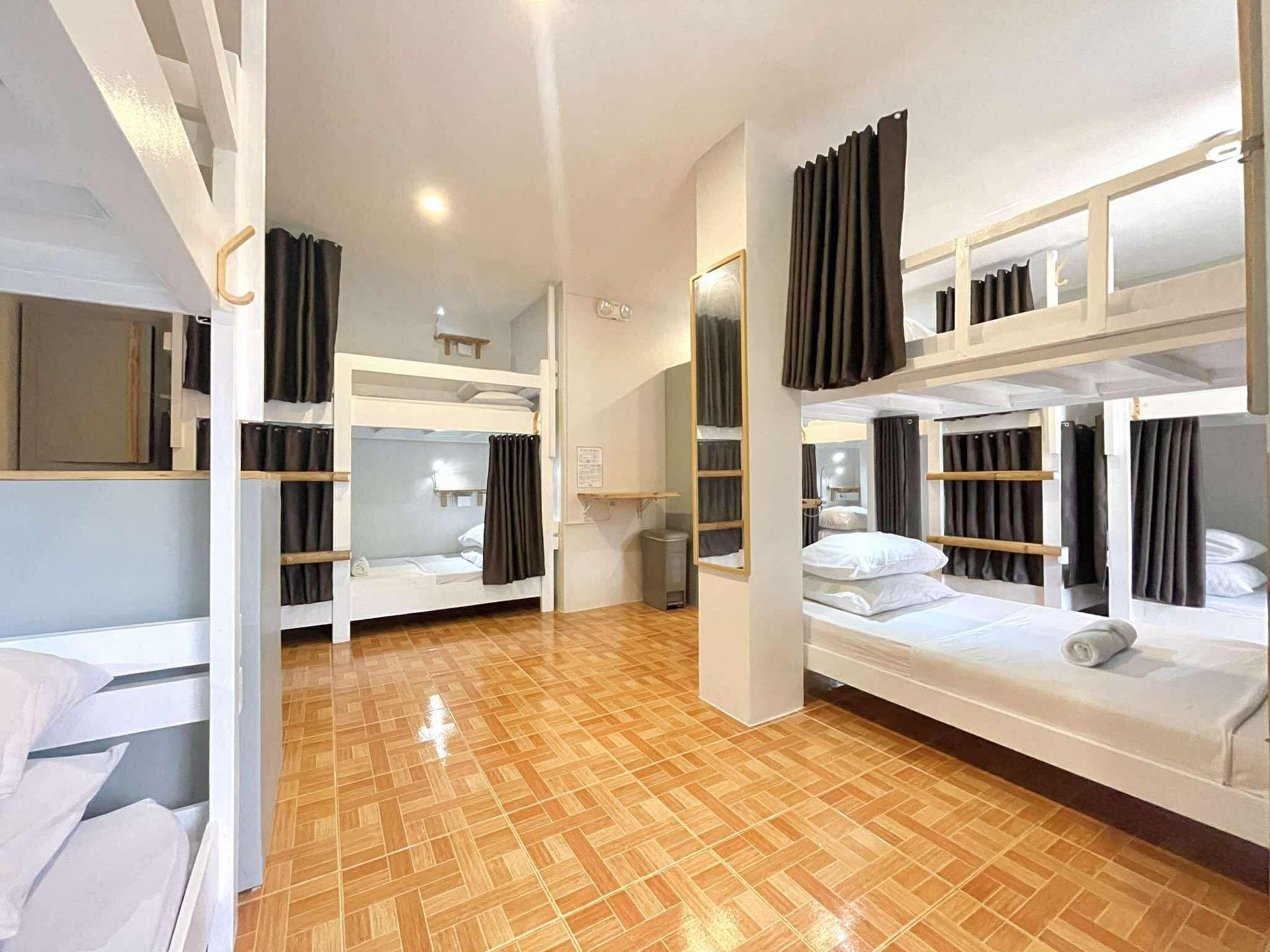 Hostel dorm room with multiple bunk beds, neutral-colored walls, and tiled floor.